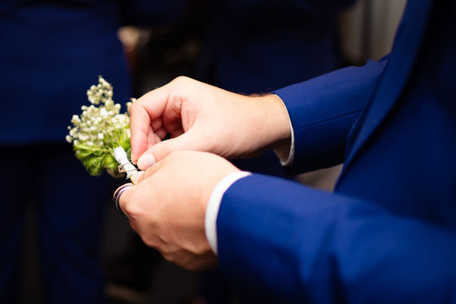 Close-up shots of boutonniere being pinned on navy blue suit.