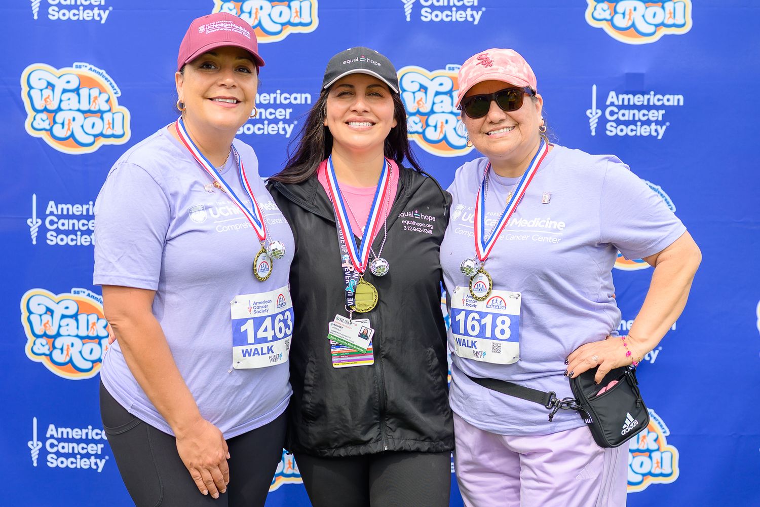 Three women with medals pose at American Cancer Society Walk & Roll event backdrop.