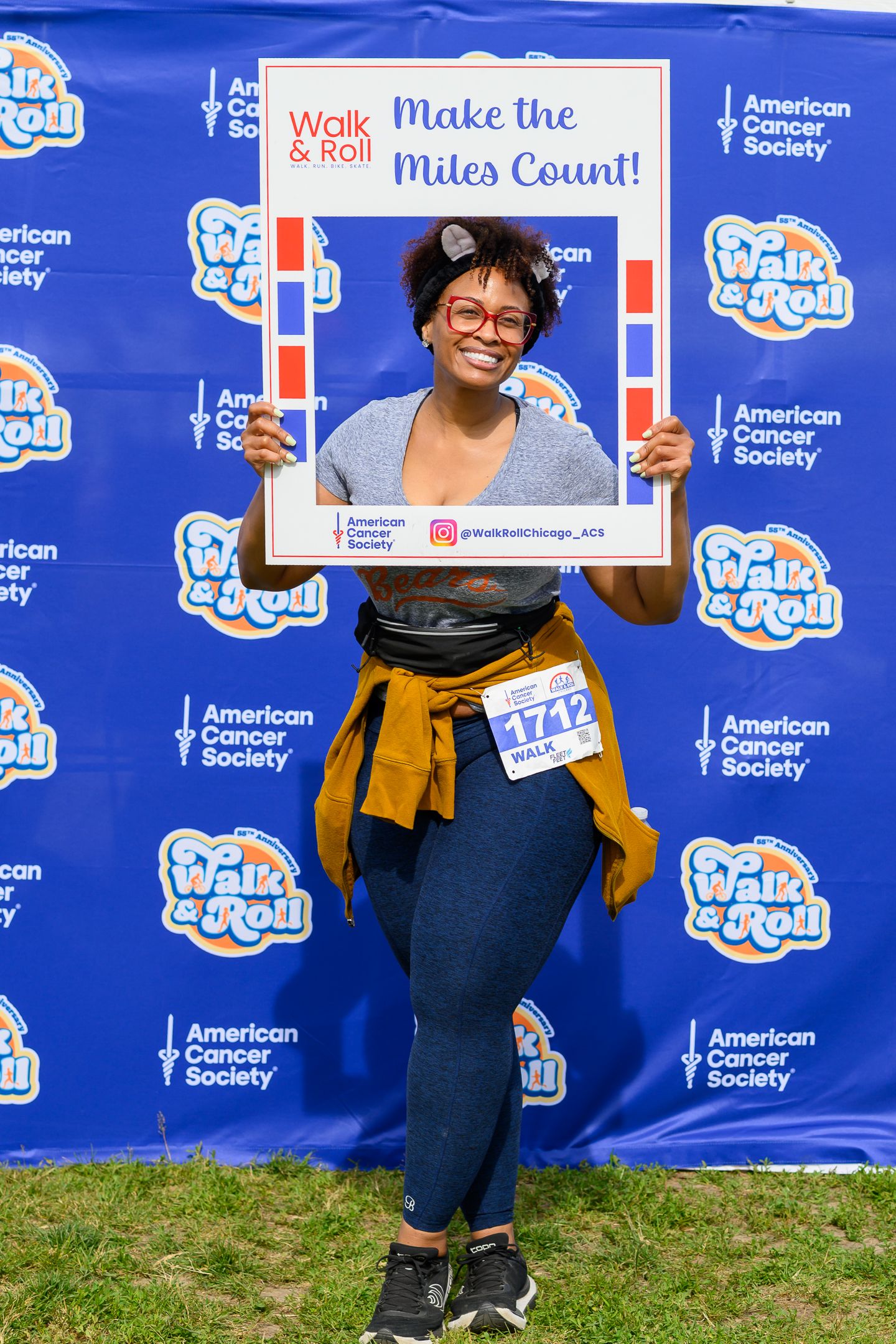 Smiling woman holds Walk & Roll Make the Miles Count photo frame at American Cancer Society charity event.