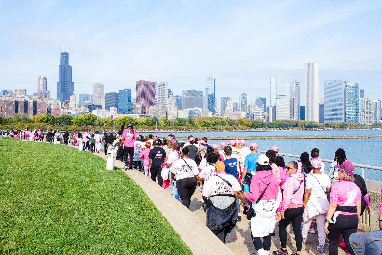 Large crowd of people walking along Chicago's lakefront trail with the city skyline visible in the background.