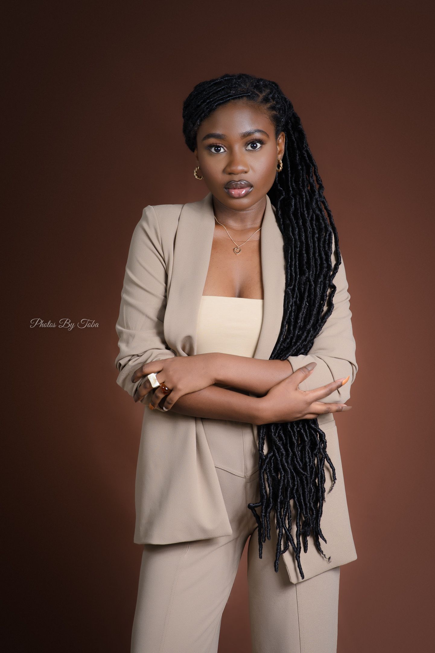 A professional studio portrait featuring a person in a beige blazer against a brown background.