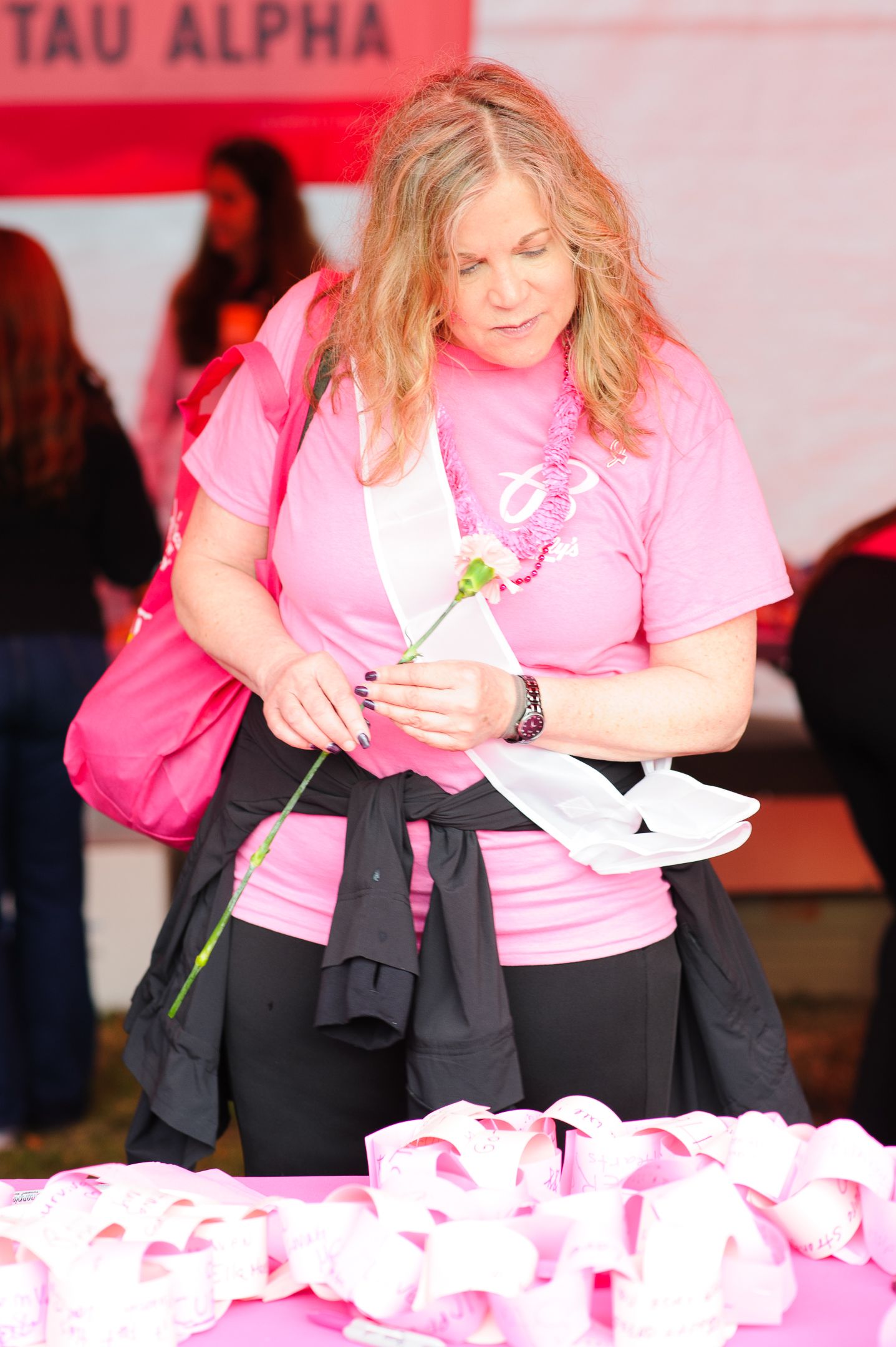 Volunteers in pink shirts place pink carnations in a memorial display during a breast cancer awareness event.