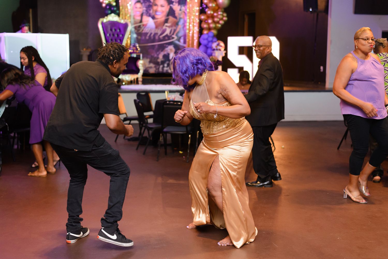 Guests dancing at an elegant 50th birthday party with purple and gold decorations in a festive ballroom.