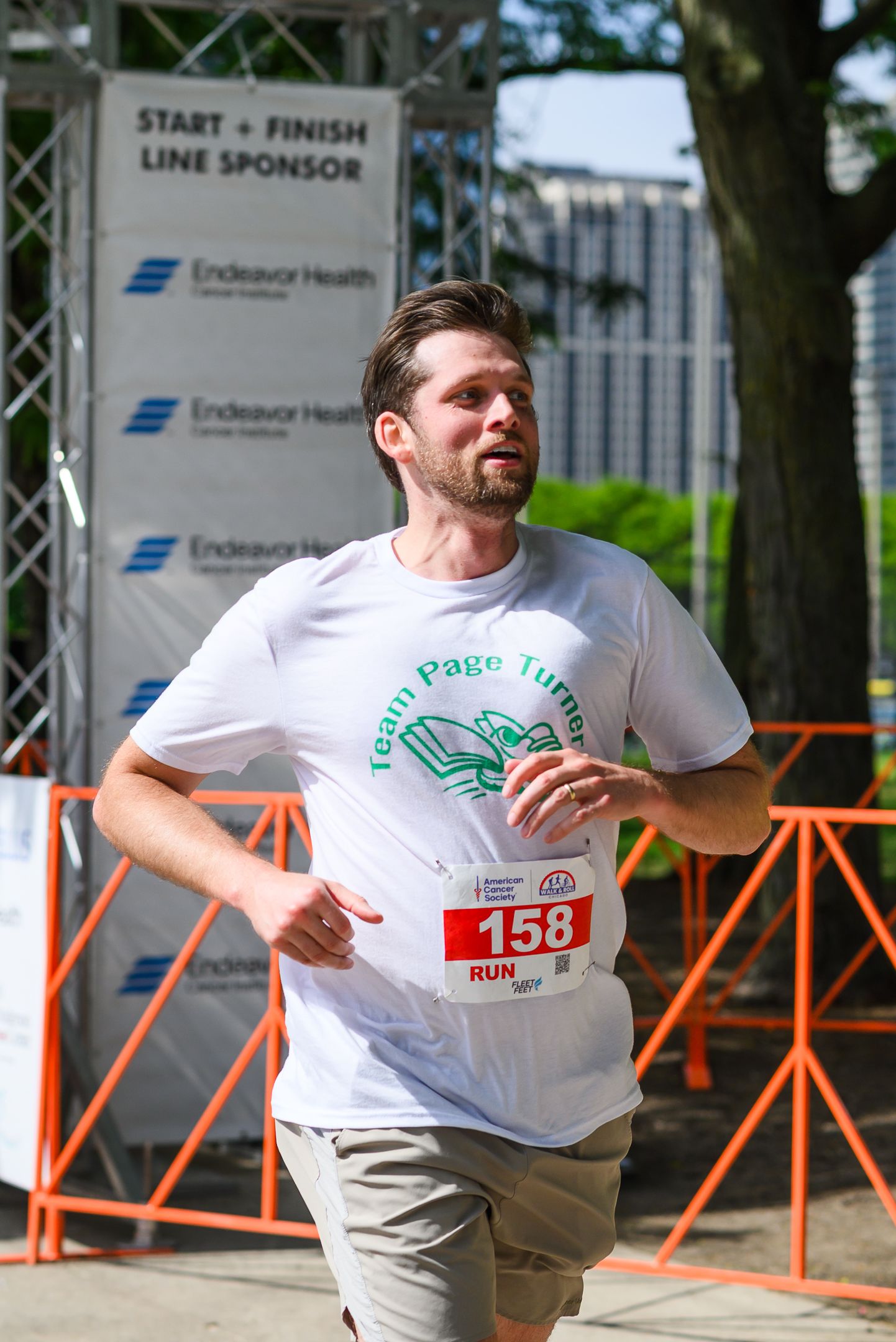 Male runner wearing Team Page Turner shirt crossing finish line at charity race event.