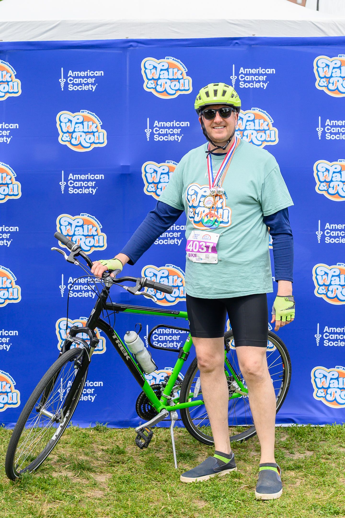 Cyclist poses with green bike at American Cancer Society Walk & Roll event, wearing medal, helmet, and race bib #4037.