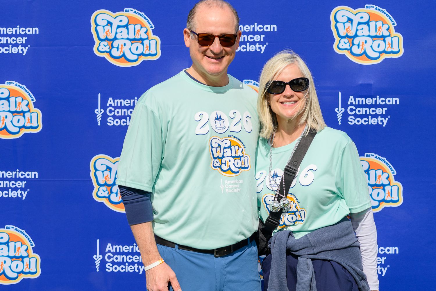 Couple in matching teal Walk & Roll 2025 shirts pose at American Cancer Society event backdrop.