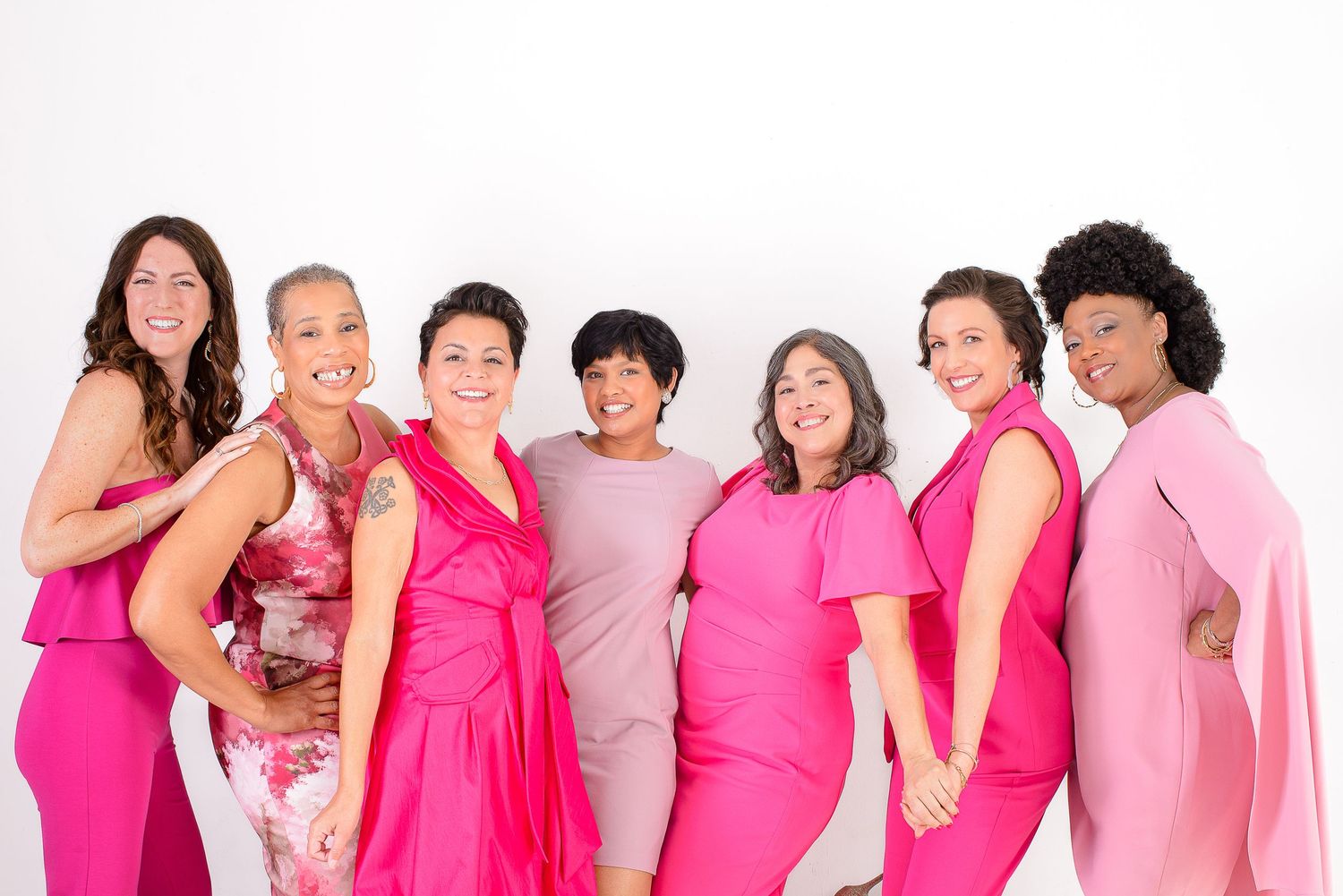 A group of people wearing various shades of pink and white clothing standing together in a row.