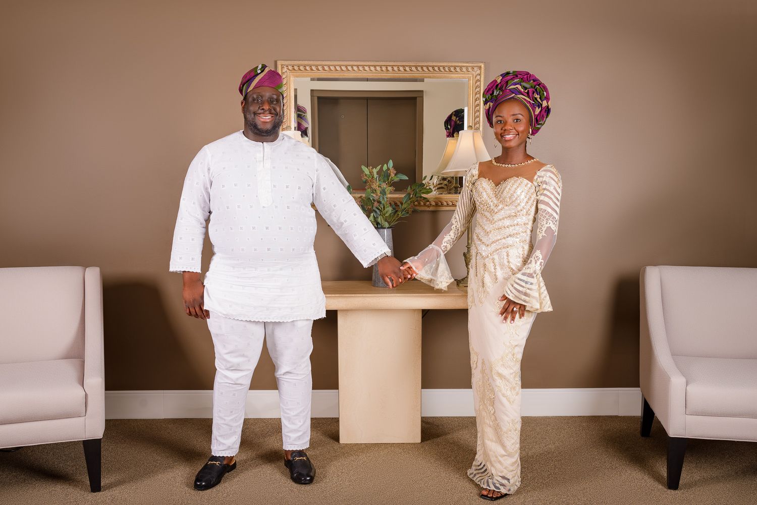 Couple in traditional Nigerian attire holding hands, man in white agbada, woman in gold lace gown with green gele headwrap.