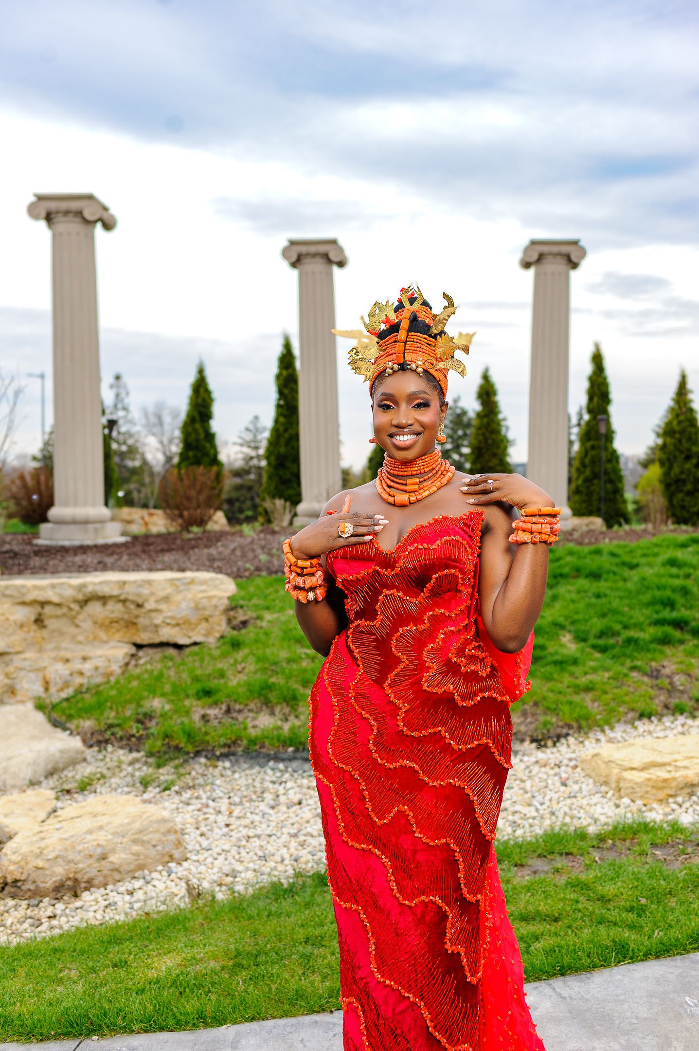 Woman in stunning red Nigerian traditional wedding dress with ornate coral beaded crown and jewelry poses outdoors.