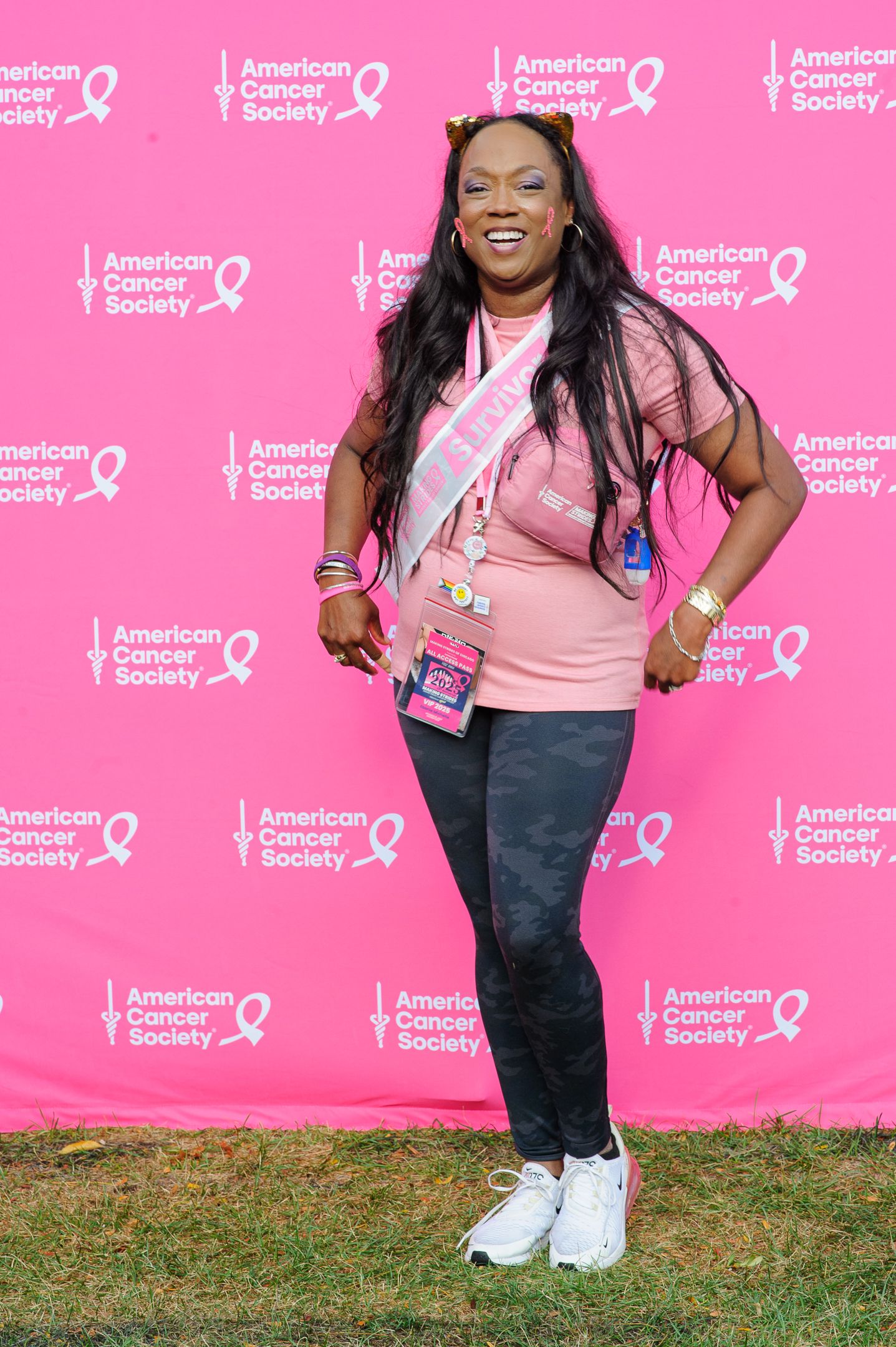 People in pink shirts and casual attire stand against a bright pink backdrop with American Cancer Society logos.