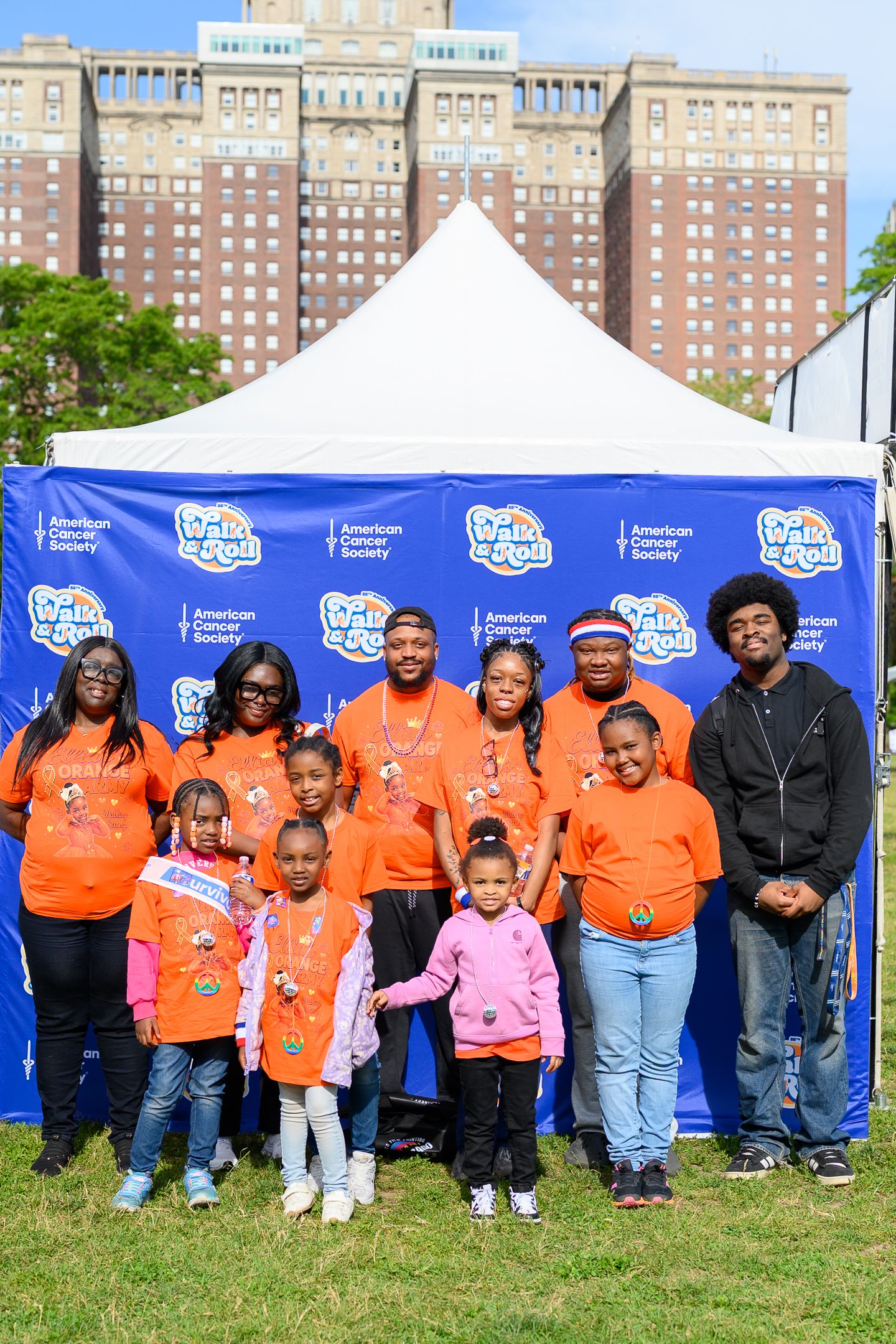 Group of people in orange shirts posing at American Cancer Society Walk event outdoors.