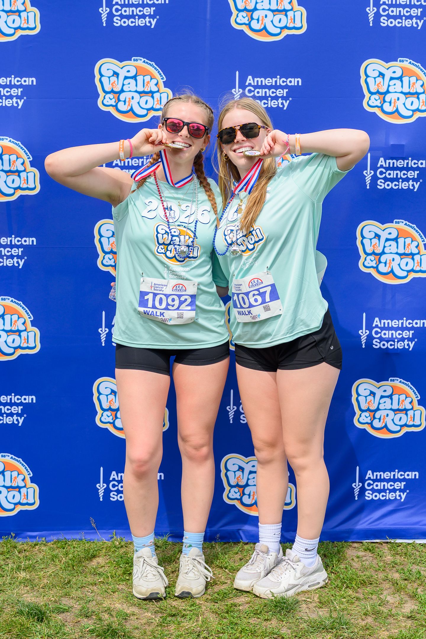 Two women in matching teal Walk & Roll American Cancer Society shirts pose with medals at charity event.