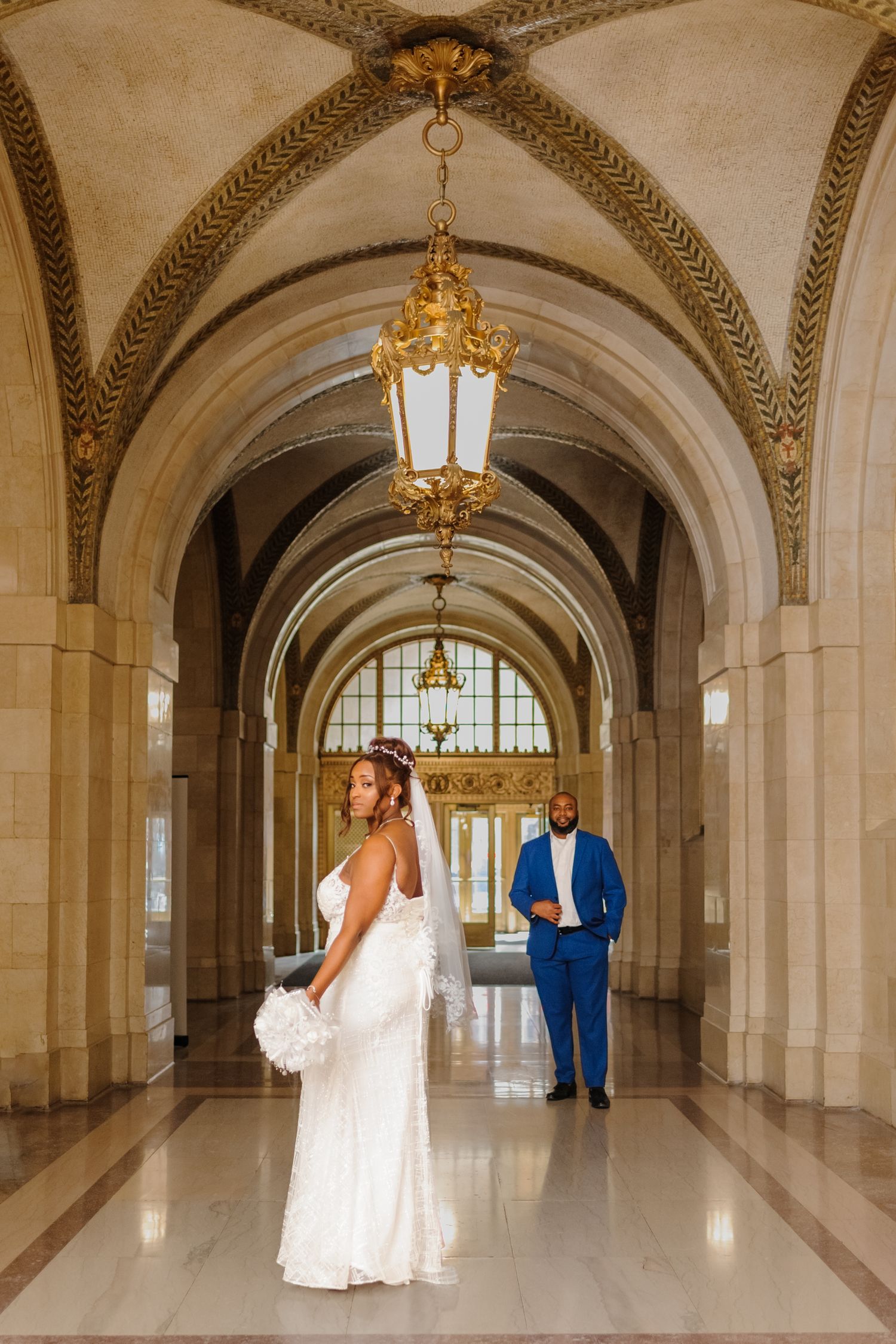 Wedding portraits captured in a grand hallway with arched ceilings and hanging chandeliers.