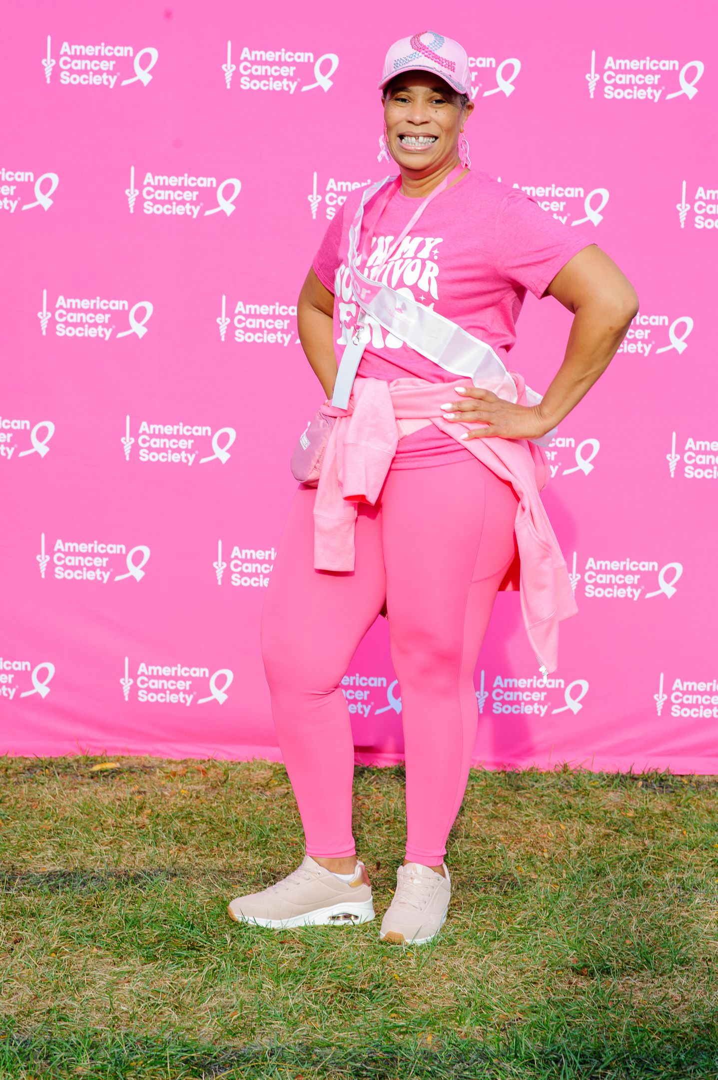 Participants wearing pink outfits pose against a bright pink American Cancer Society backdrop at a charity event.