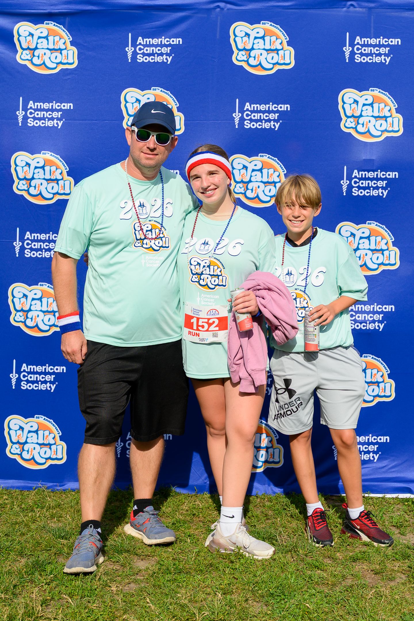 Three participants in teal Walk & Roll American Cancer Society shirts pose together at an outdoor charity fundraising event.