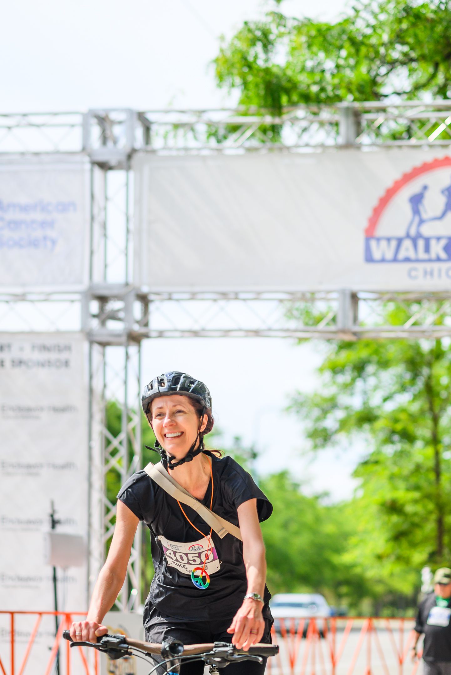 Smiling woman on bicycle crosses finish line at Walk & Roll Chicago American Cancer Society event.