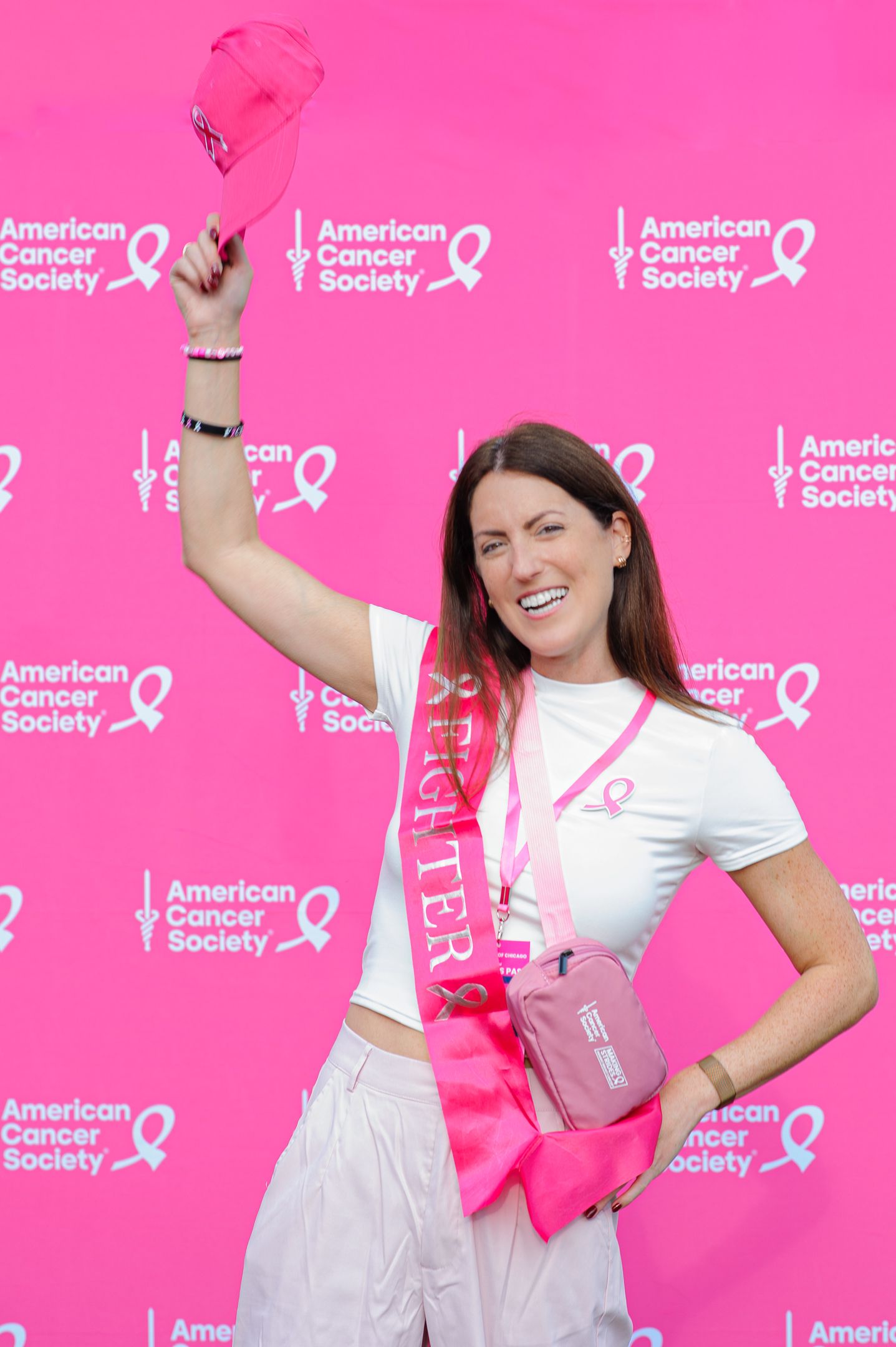 Participants pose energetically against a bright pink American Cancer Society backdrop with ribbons.