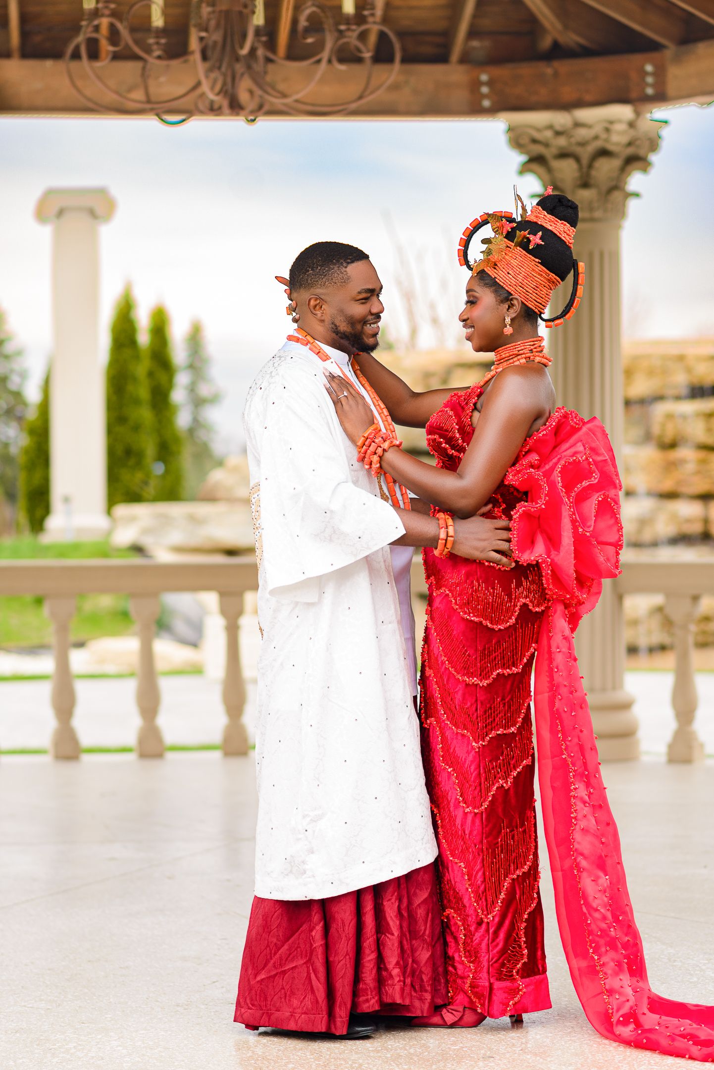 Nigerian bride and groom in vibrant traditional Urhobo wedding attire embracing under an outdoor pavilion.
