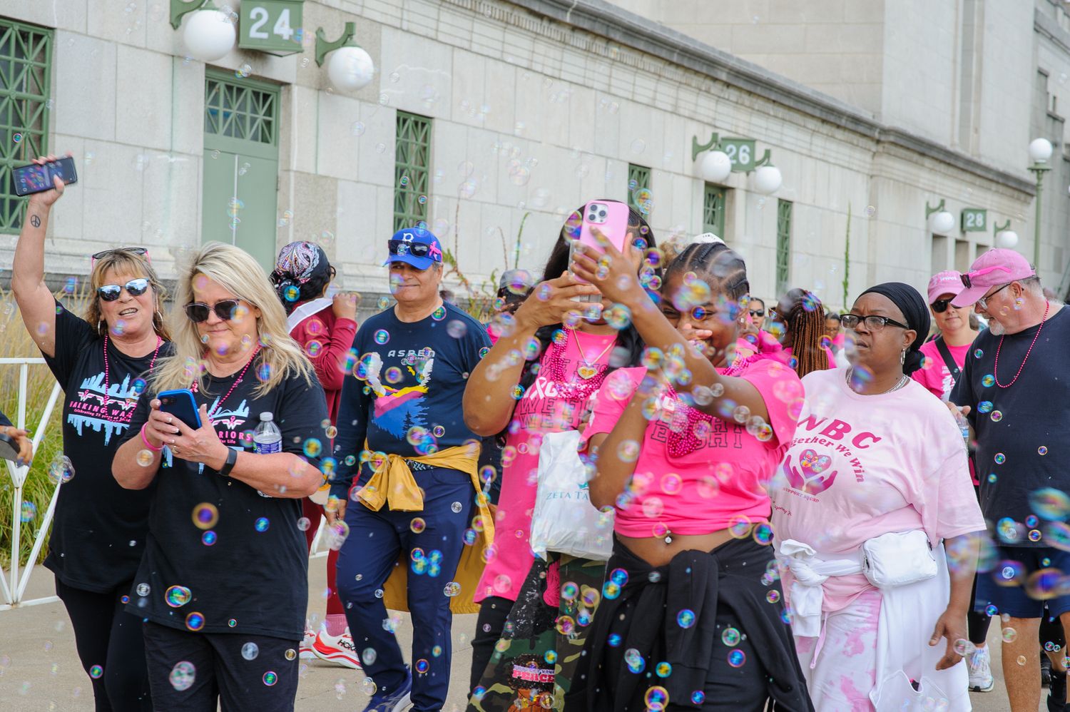 Large group of participants wearing pink and navy shirts gather at an outdoor breast cancer awareness event.