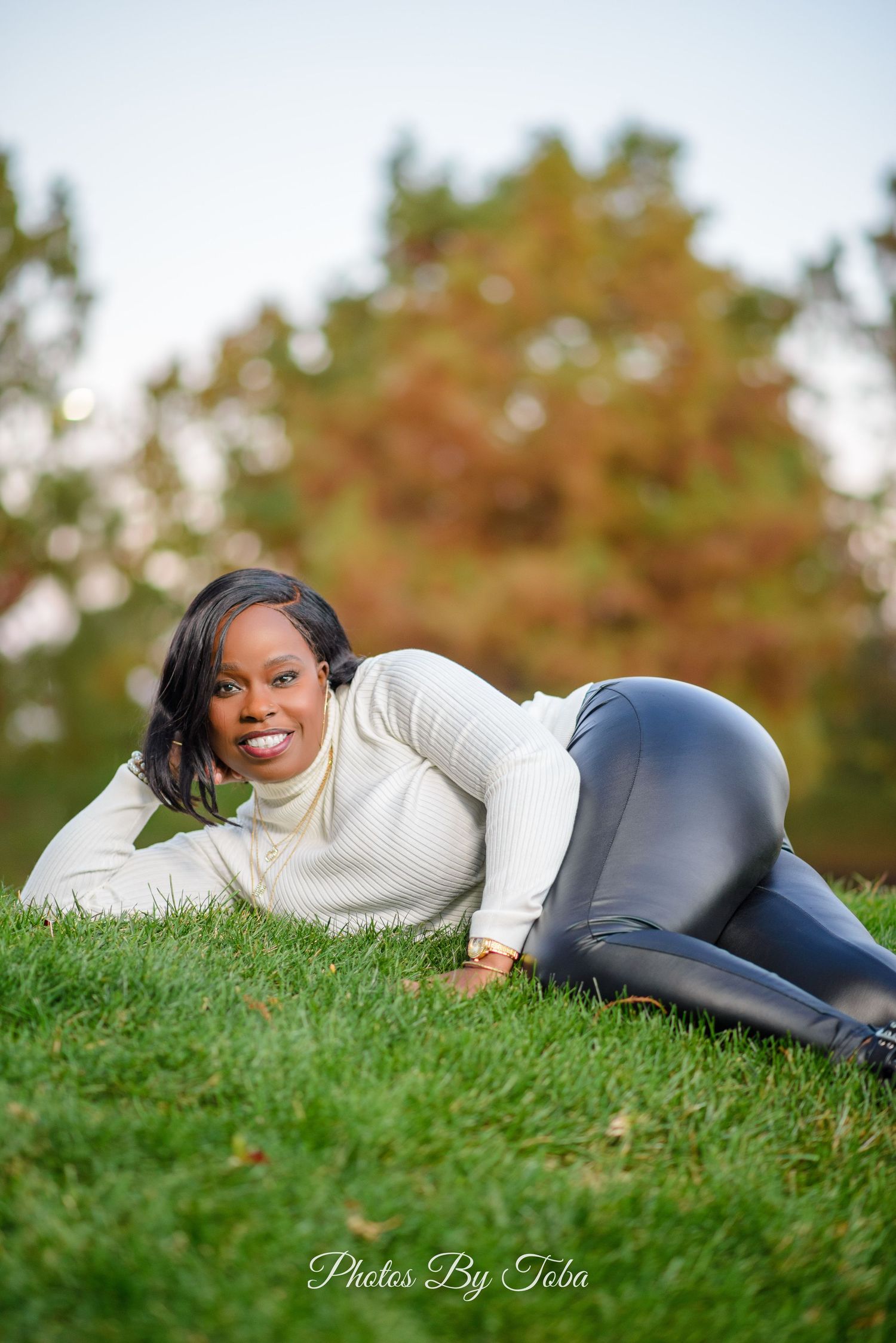 Person in white sweater laying on green grass during autumn photoshoot.