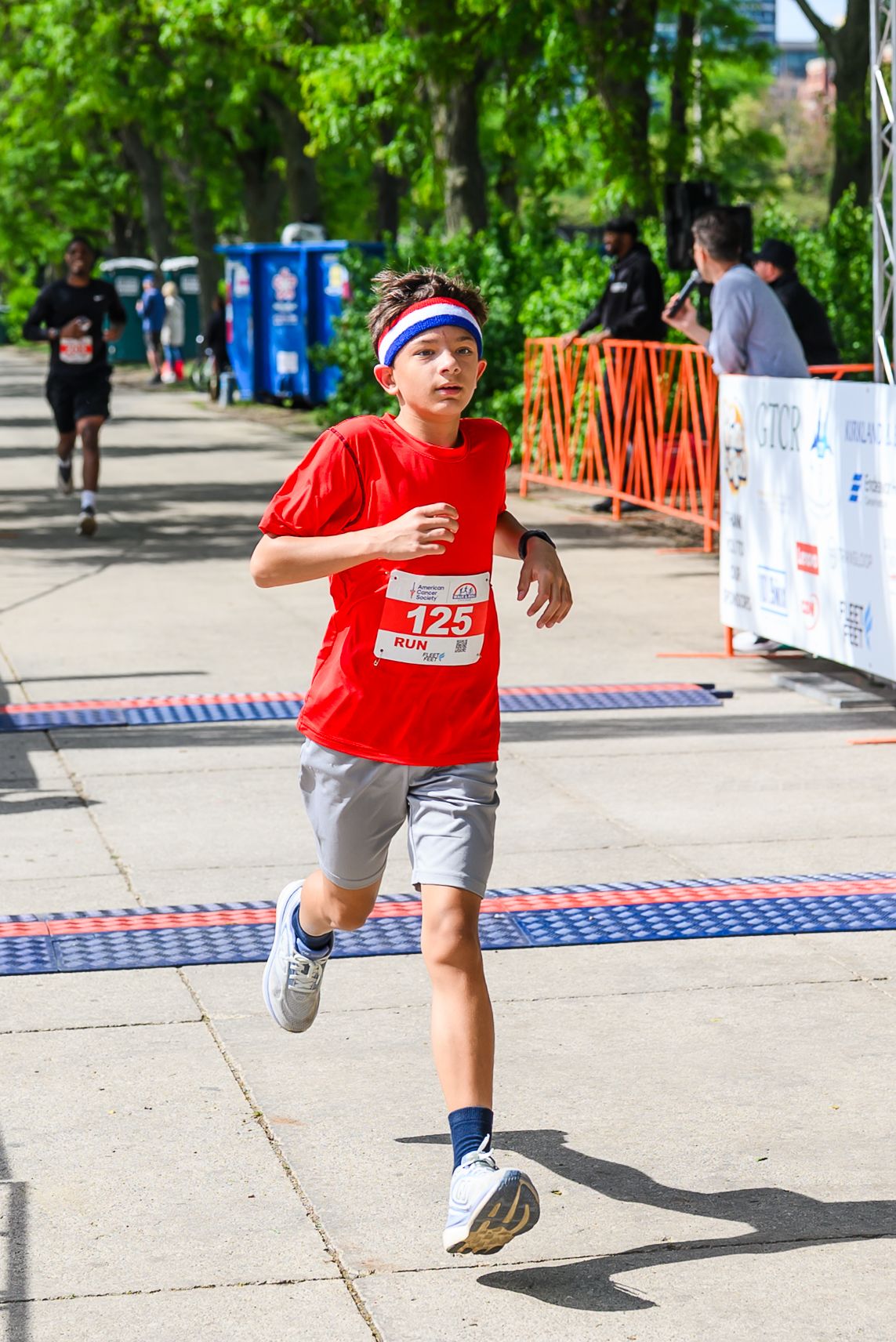 Young boy in red shirt crosses finish line wearing race bib 125 at Walk & Roll Chicago charity run.