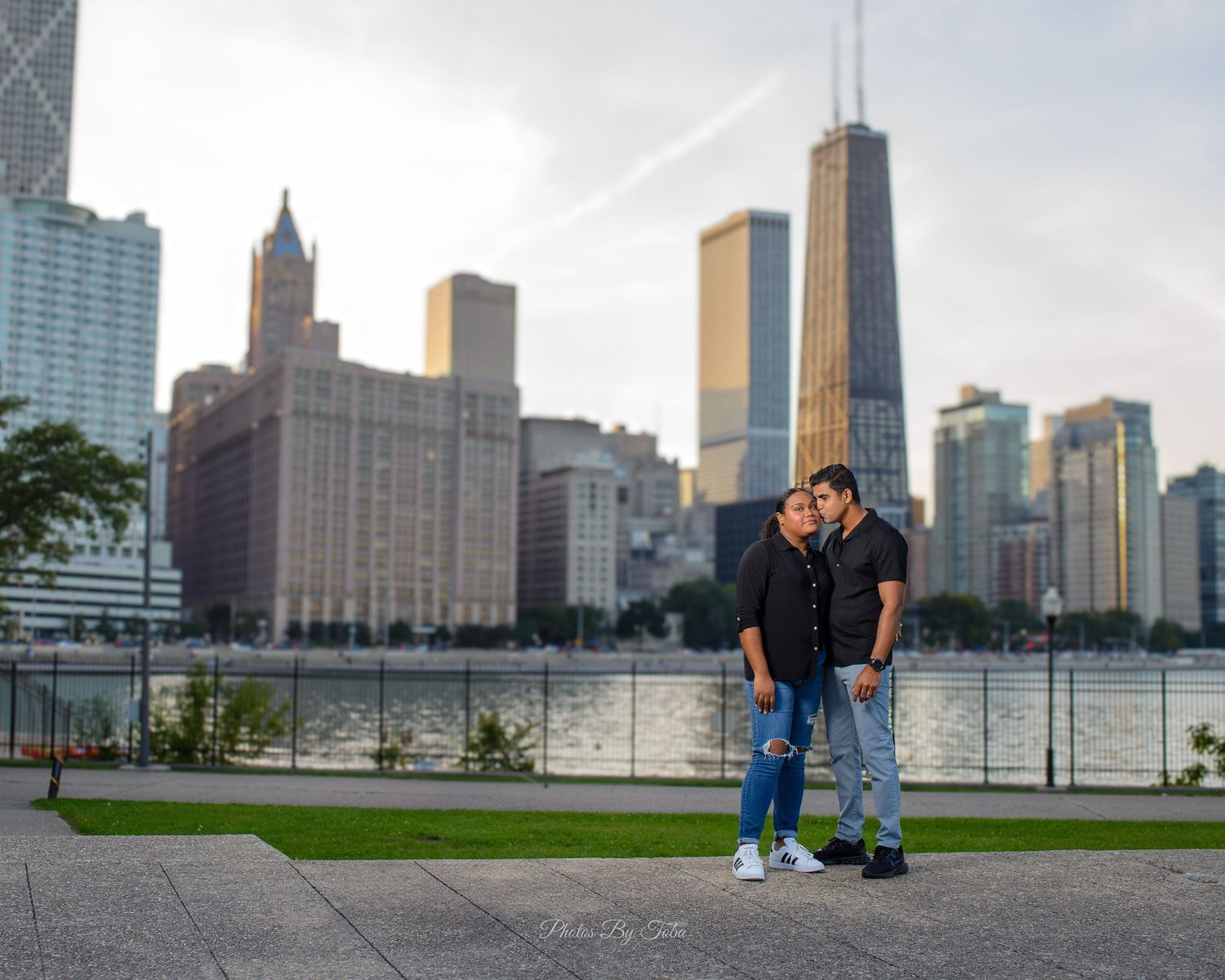 Couple embracing in front of Chicago skyline with John Hancock Center near waterfront park.