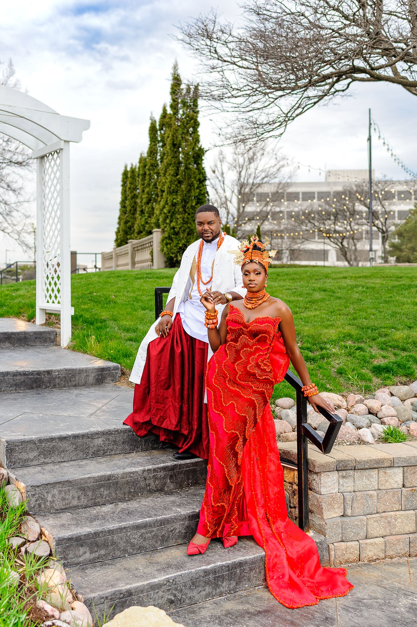 Nigerian bride and groom descending outdoor steps in vibrant red and white traditional Urhobo wedding attire.