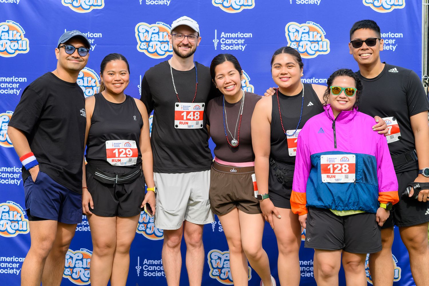 Group of seven runners posing together at an American Cancer Society Rock n Roll race event outdoors.
