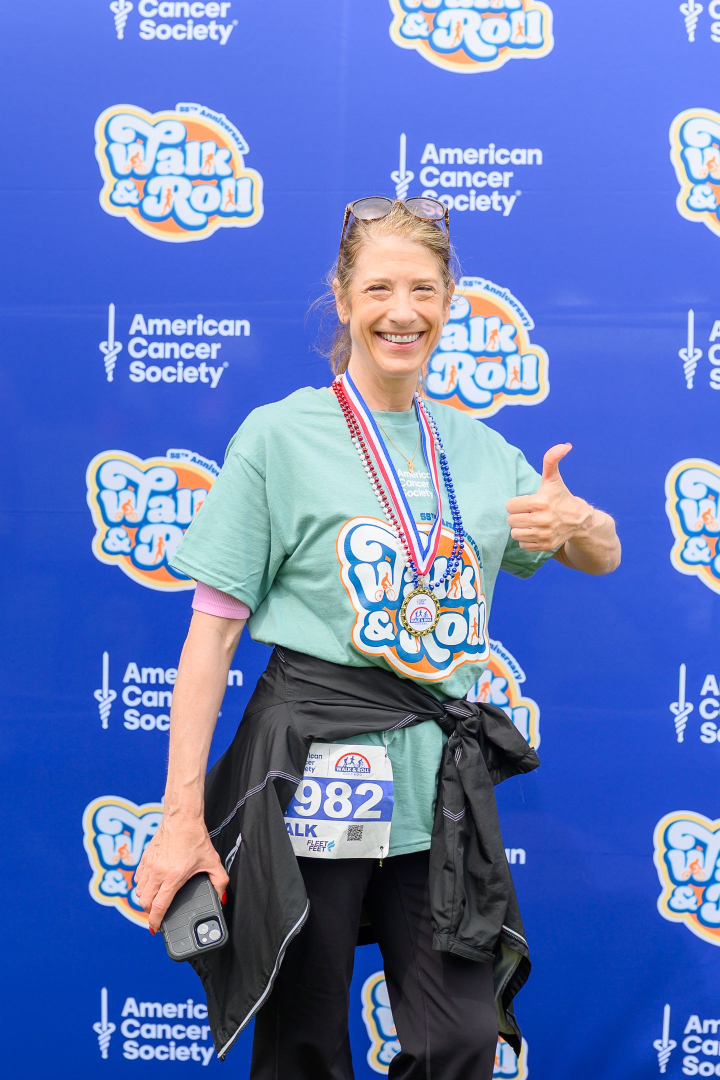 Smiling woman gives thumbs up wearing Walk & Roll Chicago medal at American Cancer Society event.
