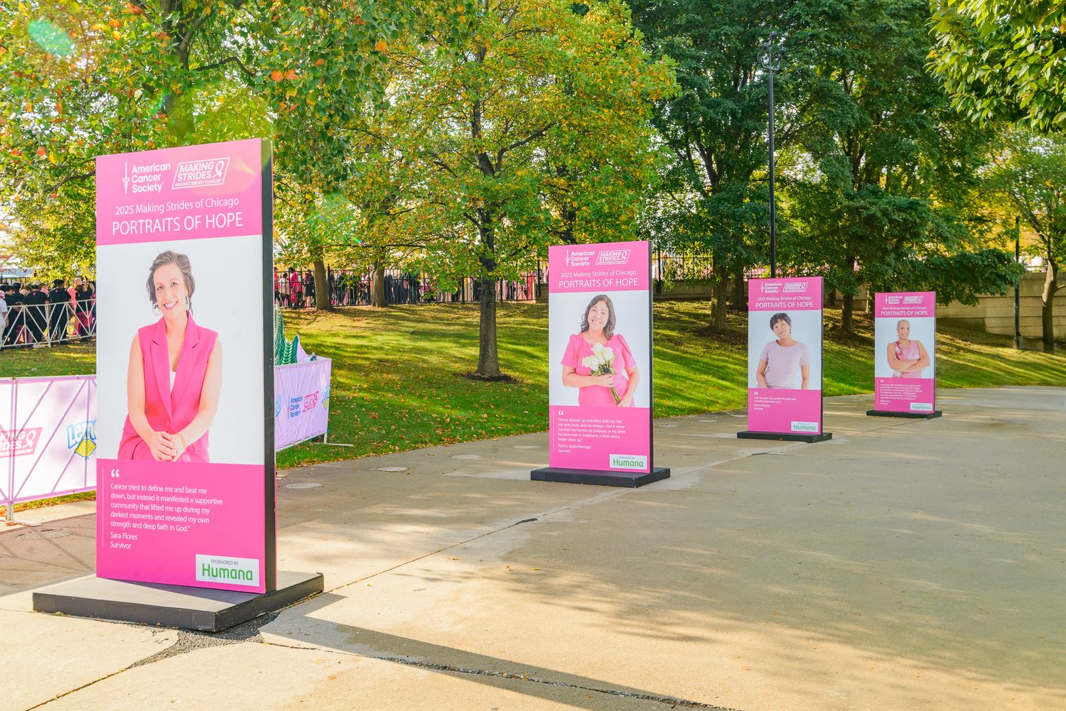 Pink informational banners line a tree-lined pathway in an outdoor park setting.