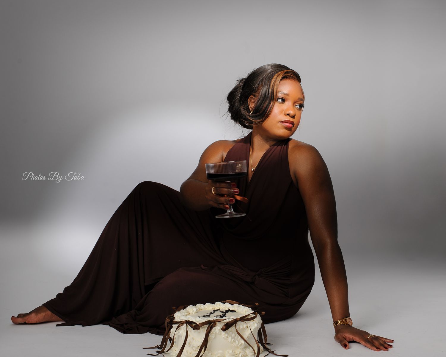 Woman in brown maxi dress sitting on floor holding red wine glass in professional studio photo shoot.