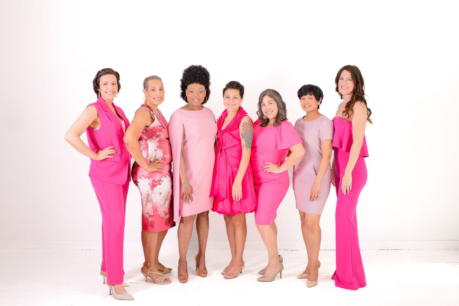 A group of people wearing pink outfits and boots pose together in a white studio setting.