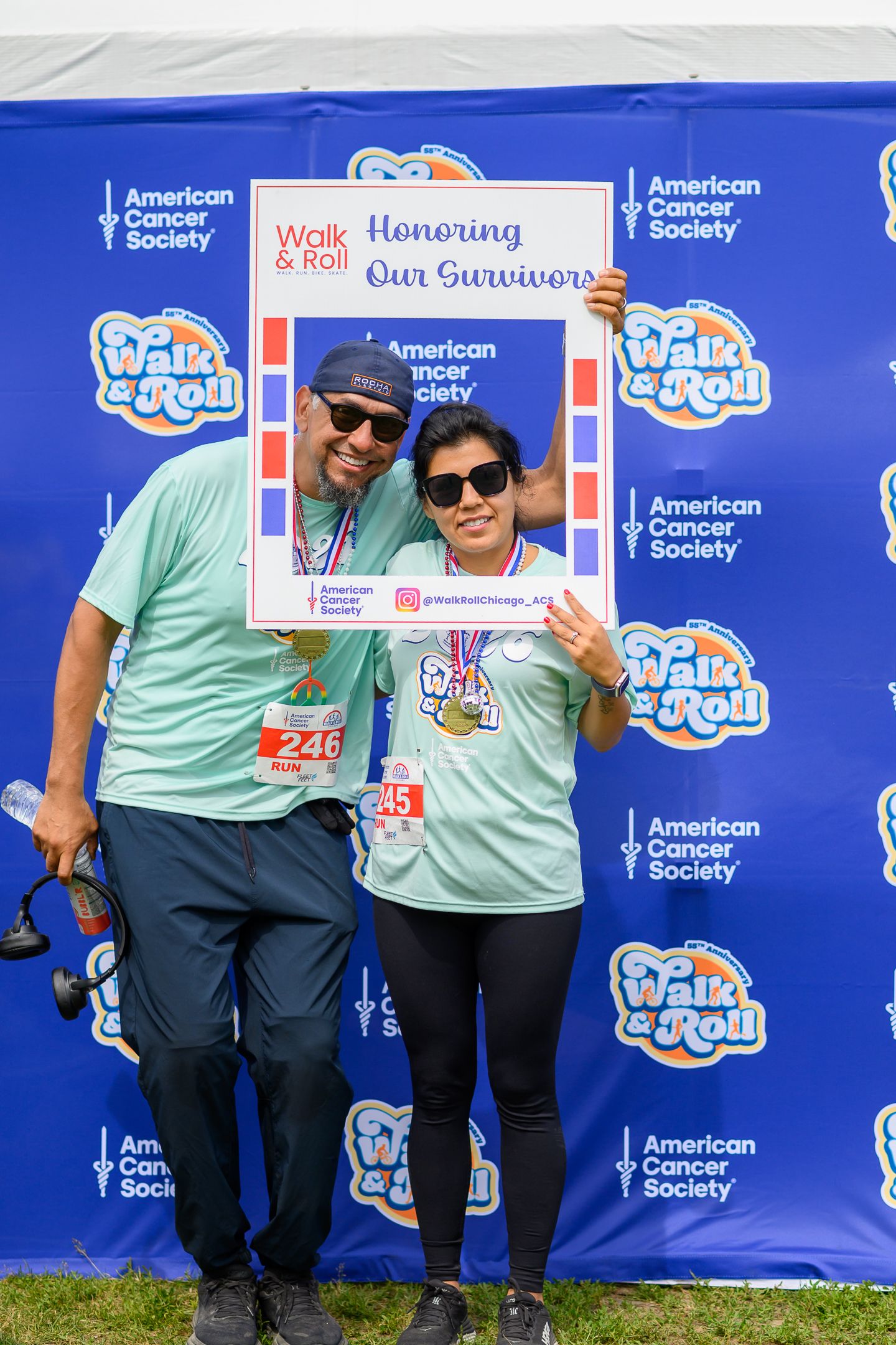 Two participants pose with an American Cancer Society Walk & Roll 'Honoring Our Survivors' photo frame at a charity event.