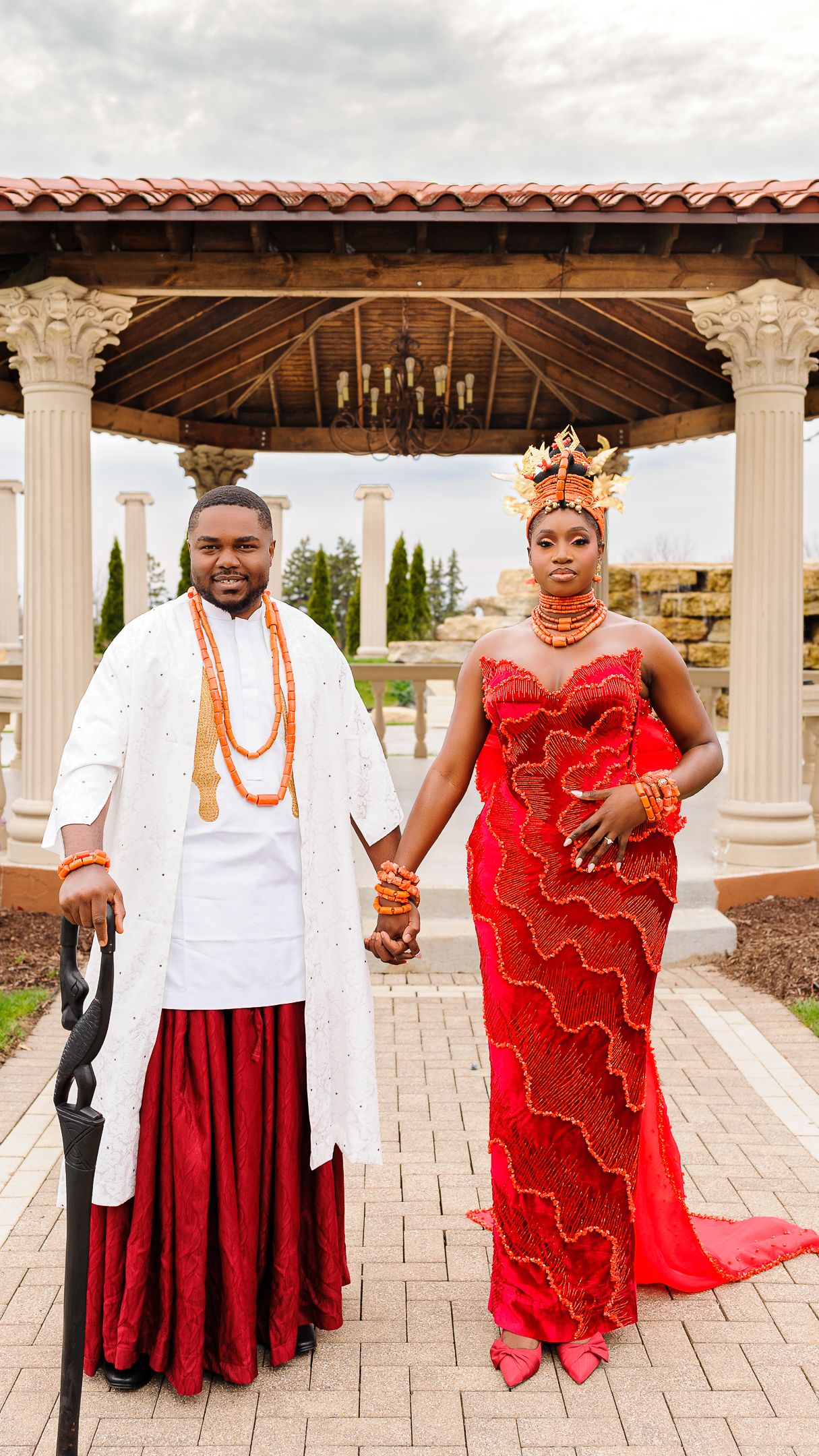 Nigerian couple in traditional Urhobo wedding attire, man in white and red, woman in red lace gown with crown.