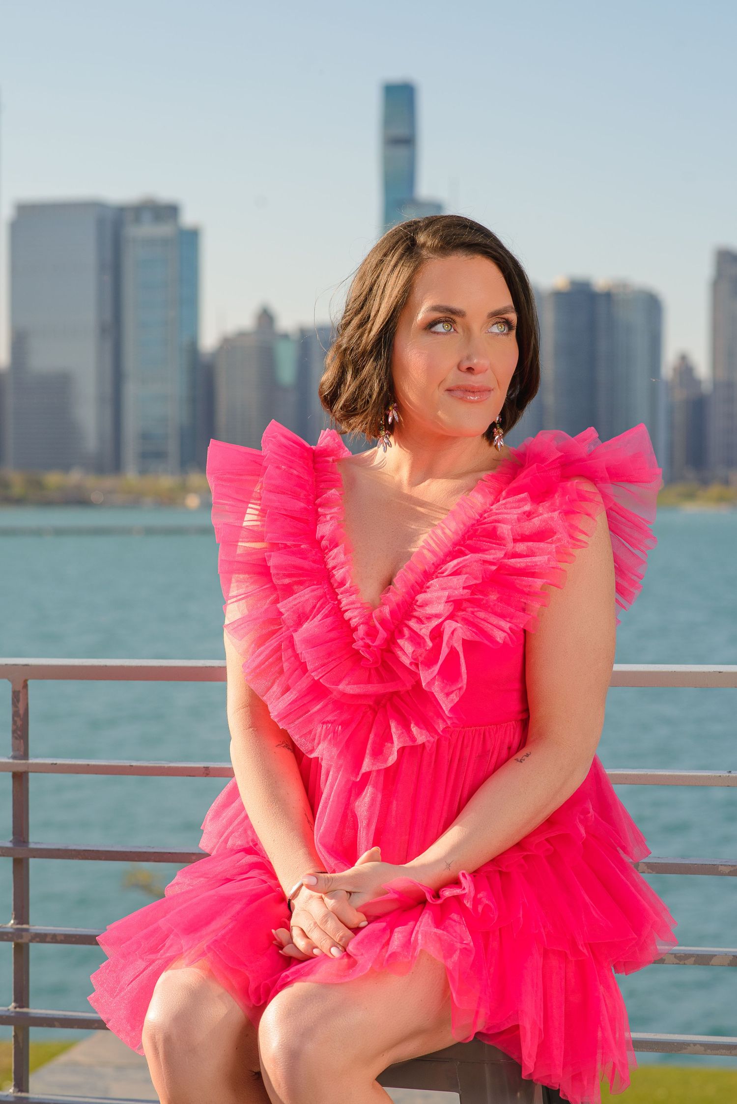 A woman in a vibrant hot pink tulle dress poses by the Chicago skyline and Lake Michigan waterfront.