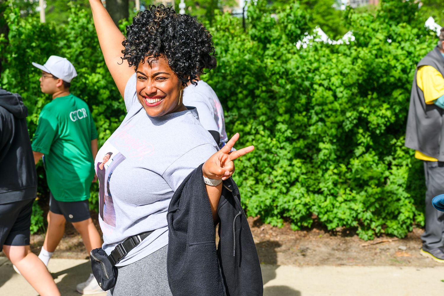 Joyful woman flashing peace sign and raising arm while participating in outdoor charity walk event.