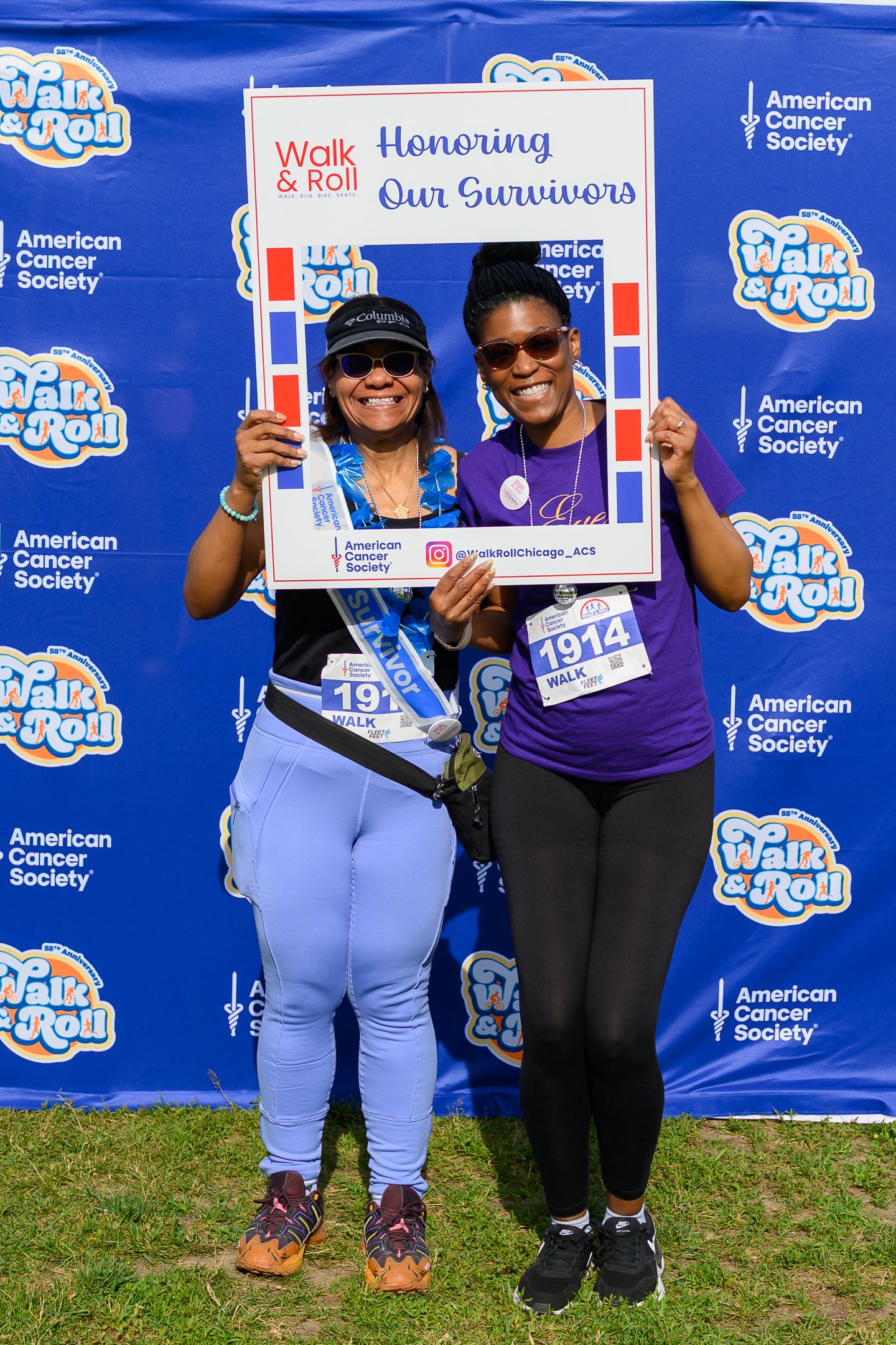 Two women smile holding an Honoring Our Survivors frame at the American Cancer Society Walk & Roll charity event.