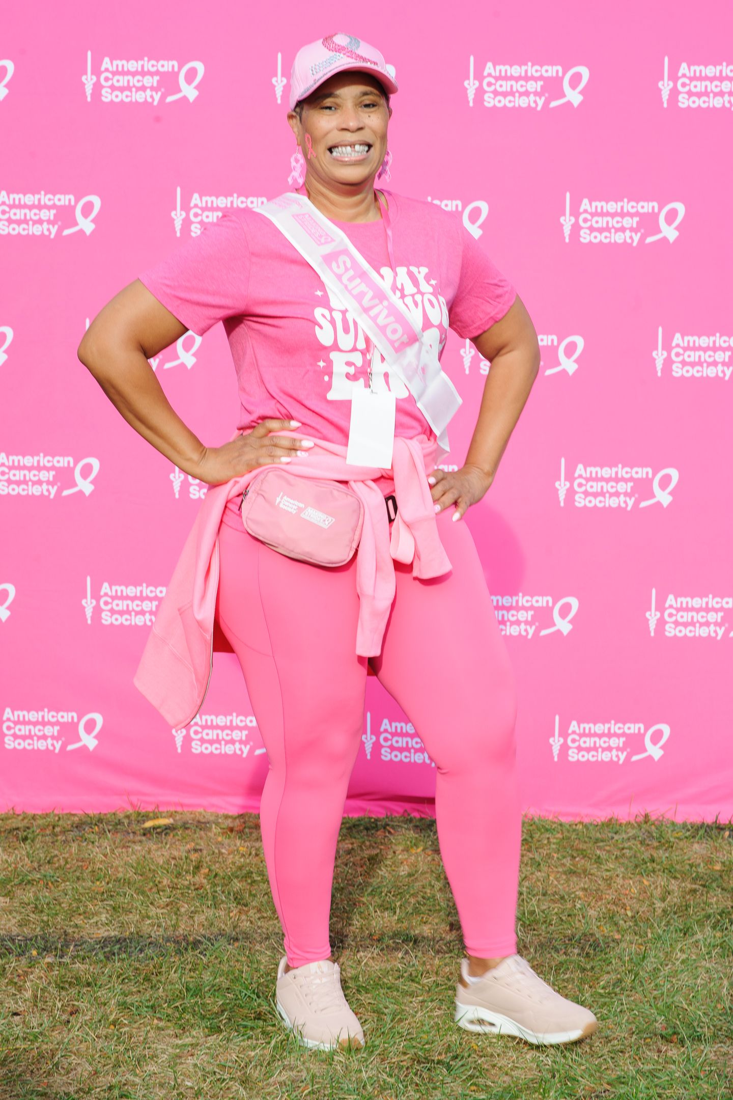 People wearing pink outfits pose energetically against a pink American Cancer Society backdrop.