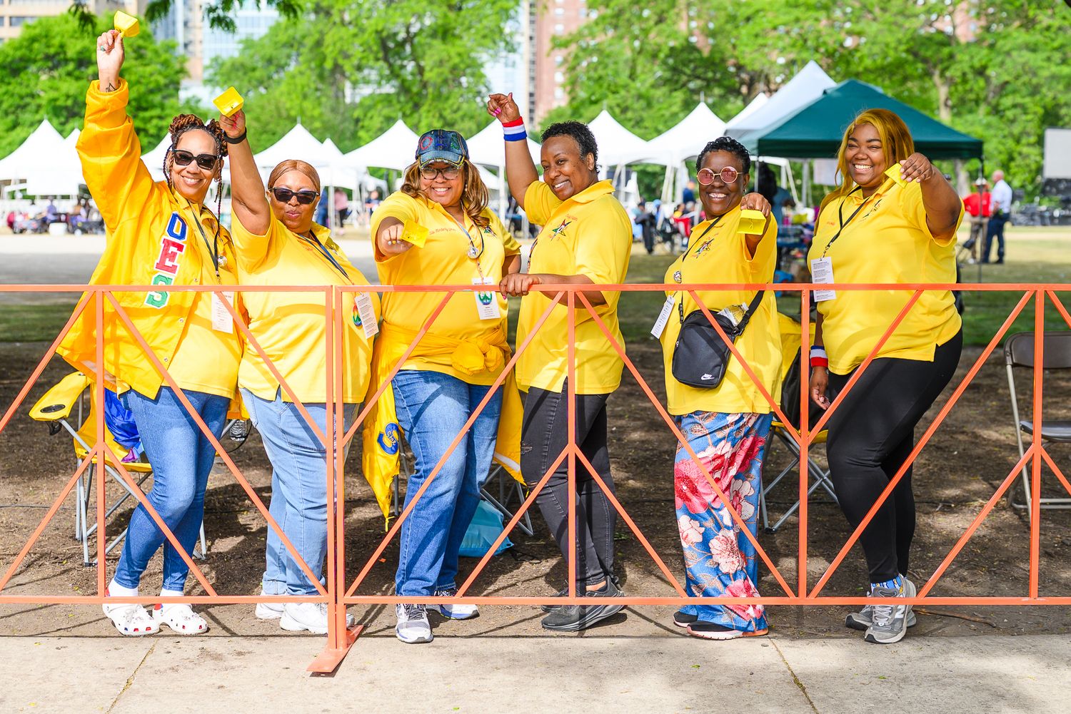 Group of six women in matching yellow jackets pose together at an outdoor American Cancer Society charity event.