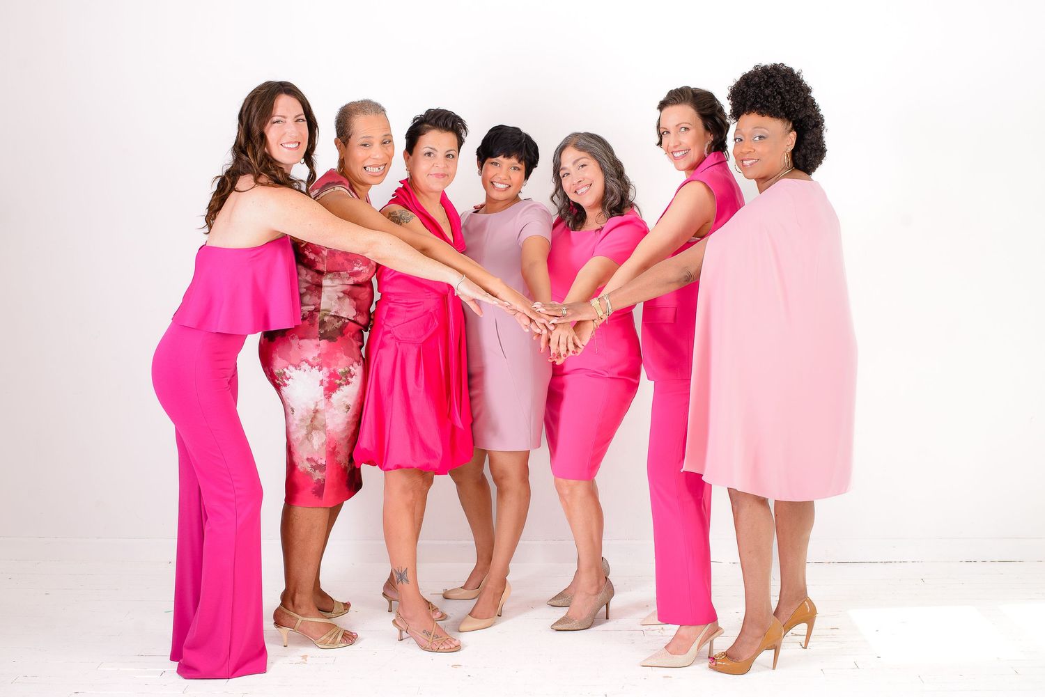 A group of people wearing pink and white outfits pose together in a studio setting.