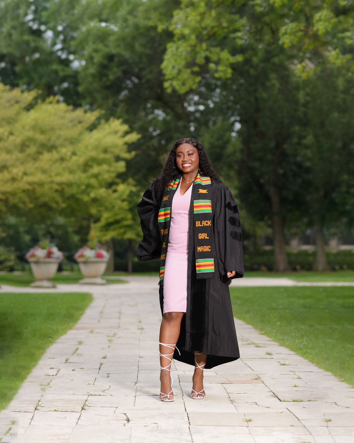 Outdoor graduation photos on a stone pathway surrounded by green trees and landscaping.