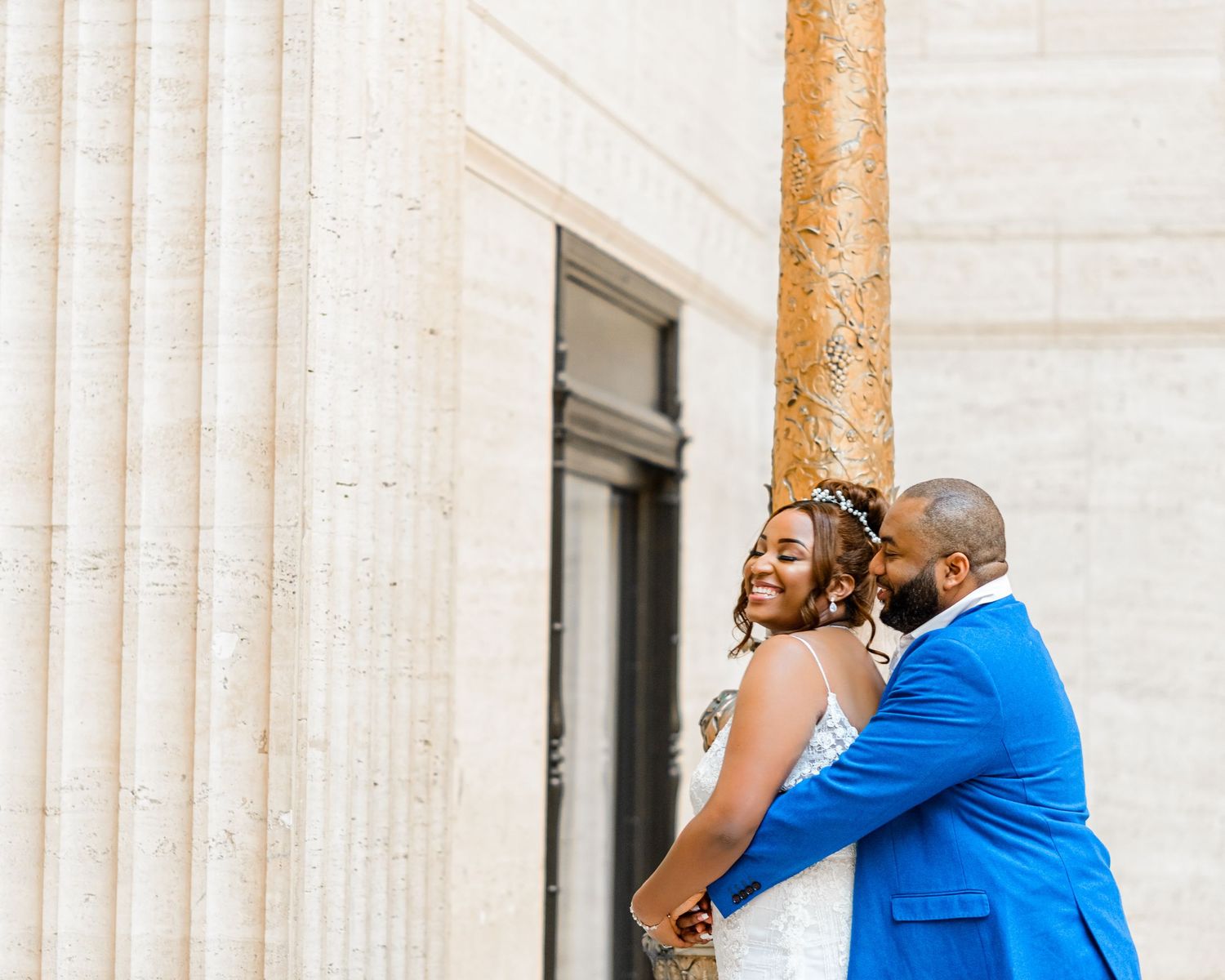 Wedding couple poses against classical stone columns in natural light.