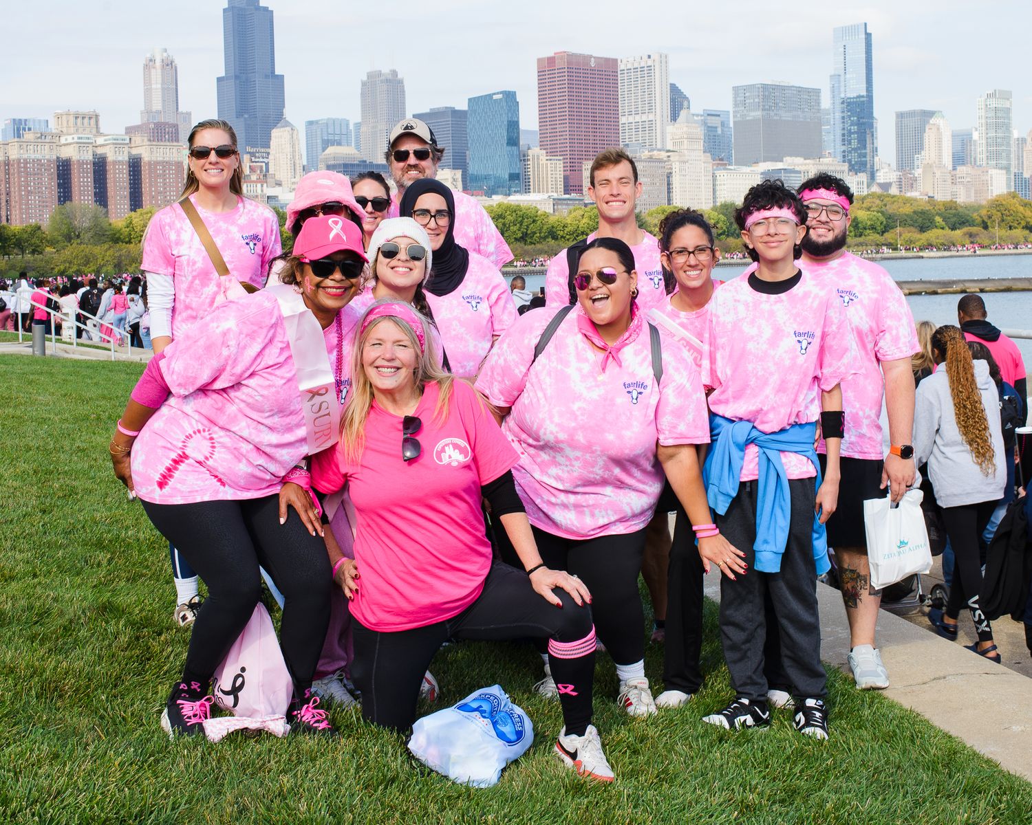 A group wearing pink shirts participates in a charity walk event with a city skyline in the background.