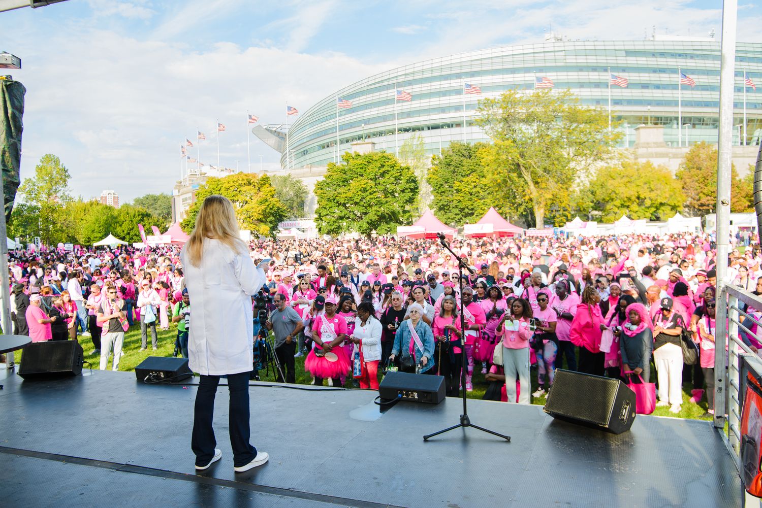 A large crowd wearing pink shirts gathers outdoors for a breast cancer awareness event on a sunny day.