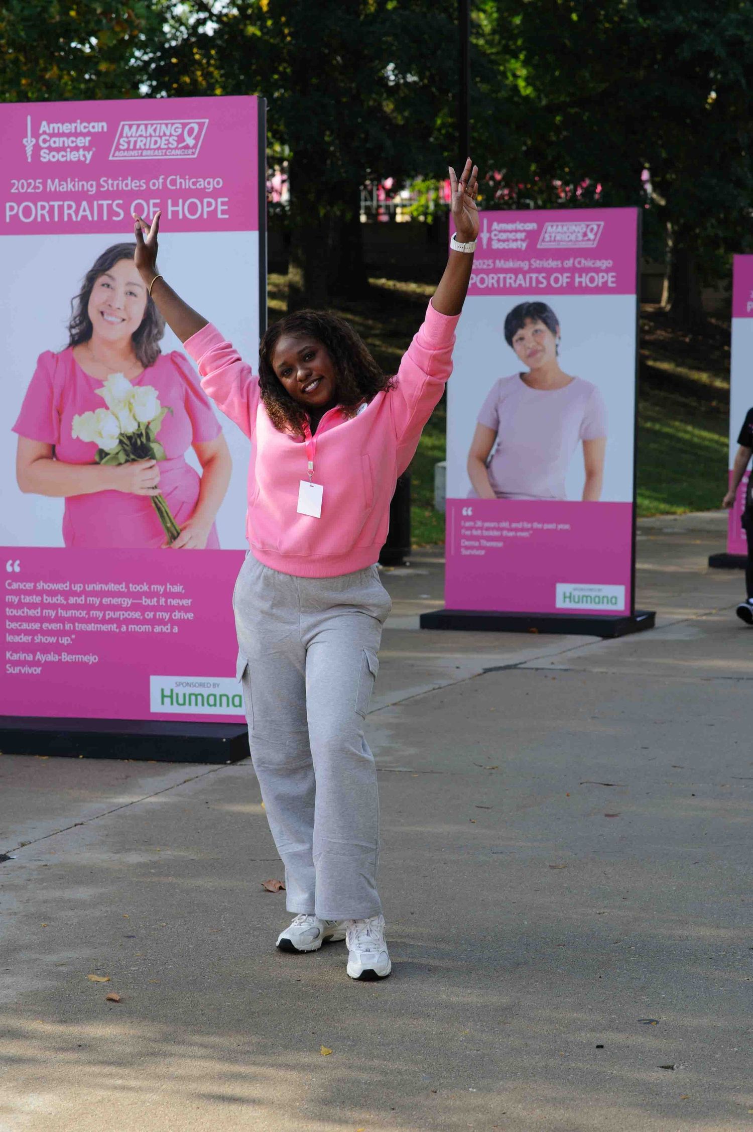A series of pink promotional banners displayed outdoors with someone in a pink sweater and gray pants posing in front.