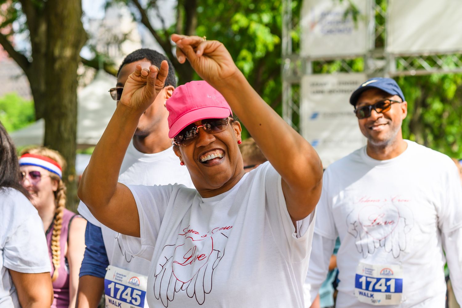 Joyful woman in pink cap and race bib 1745 dancing at charity run event outdoors.