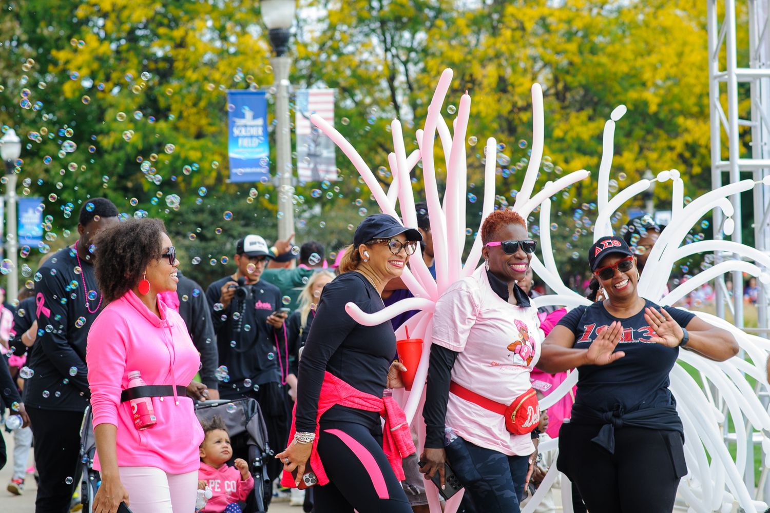 Crowd of people in pink shirts celebrating at an outdoor charity event with white pillars in background.