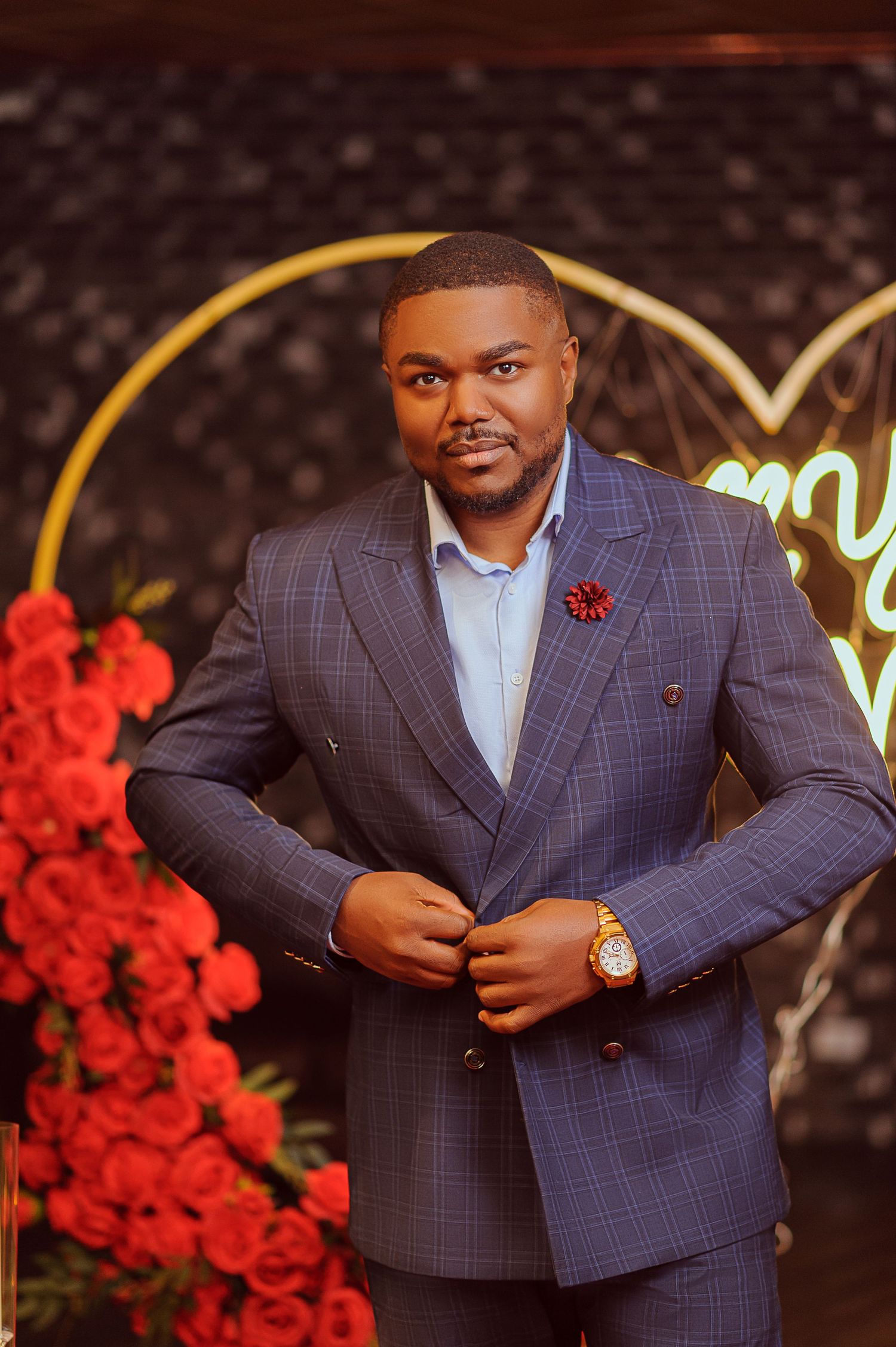 Stylish man in blue plaid double-breasted suit posing at a romantic rose-decorated proposal venue.