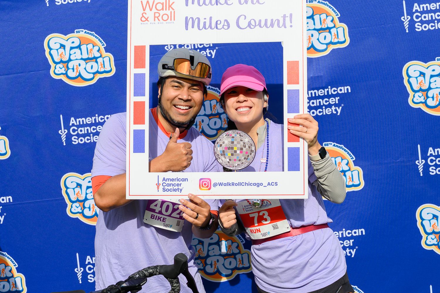 Two participants smile at American Cancer Society Walk & Roll event, posing with a decorative frame outdoors.