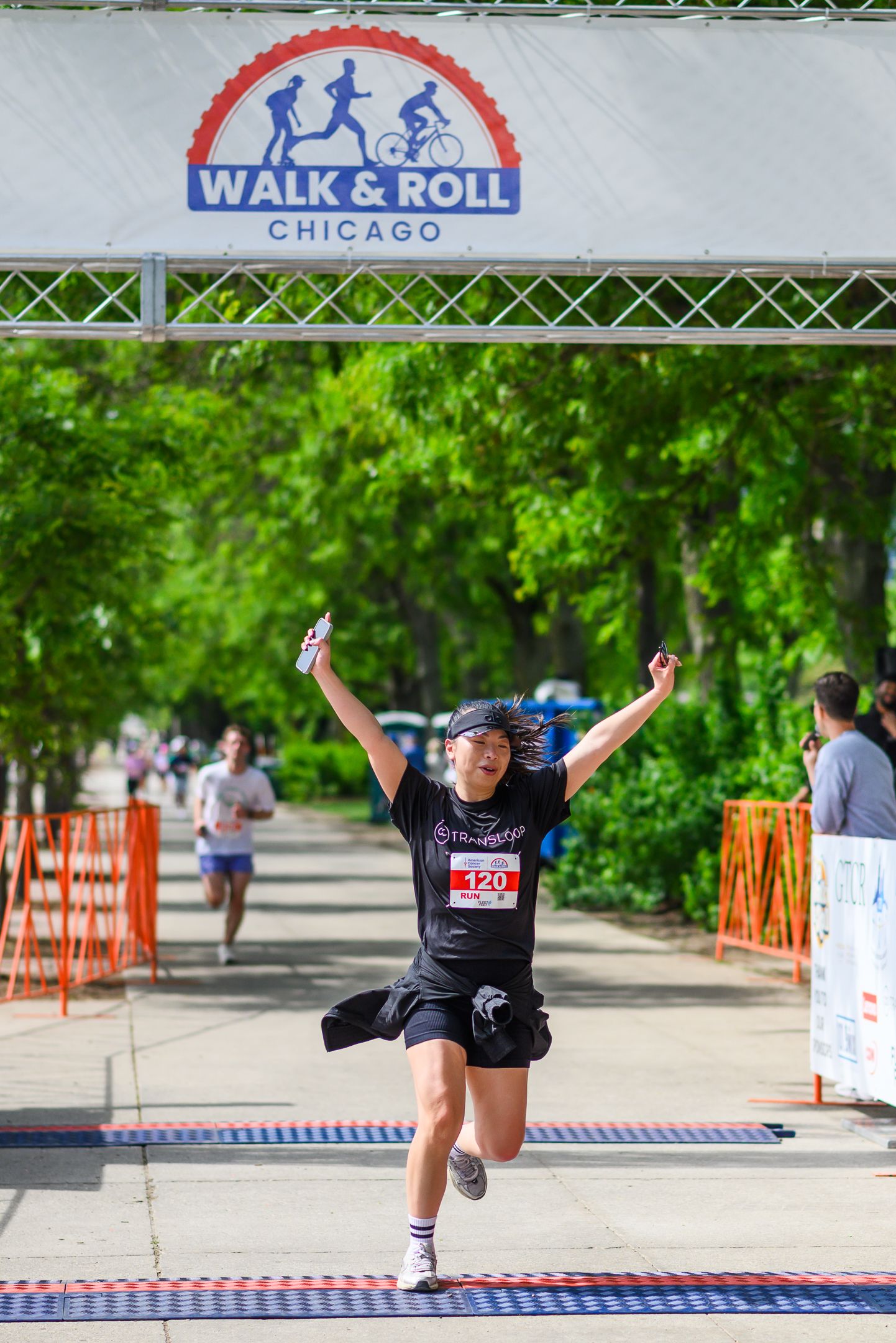 Excited female runner crosses finish line at Walk & Roll Chicago charity race with arms raised.